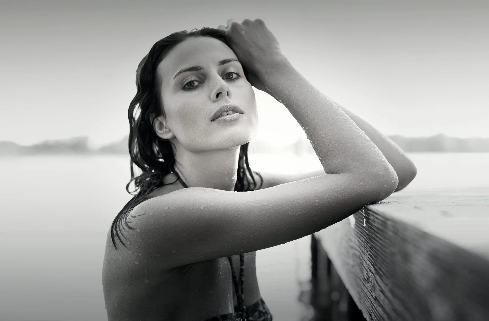 eine Frau im Bikini steht in einem See und lehnt sich mit den Armen an einem Steg an