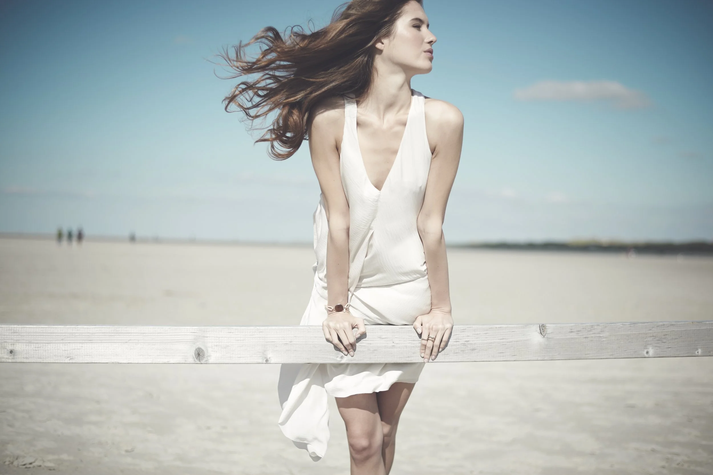 Ein Modefoto einer jungen Frau am Strand von St. Peter Ording, die Haare wehen im Wind
