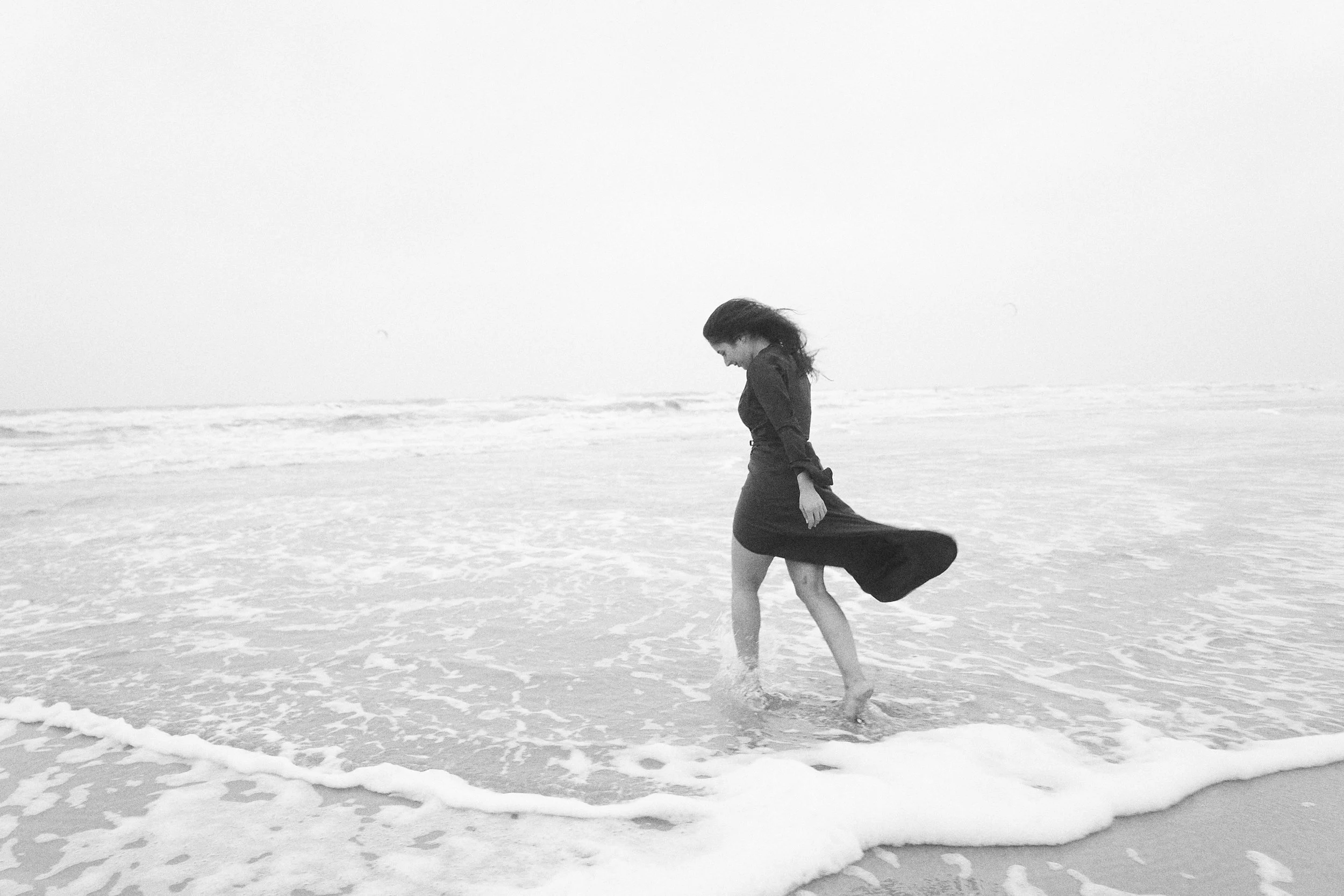 Frau in schwarzem Kleid läuft am Strand im Wasser