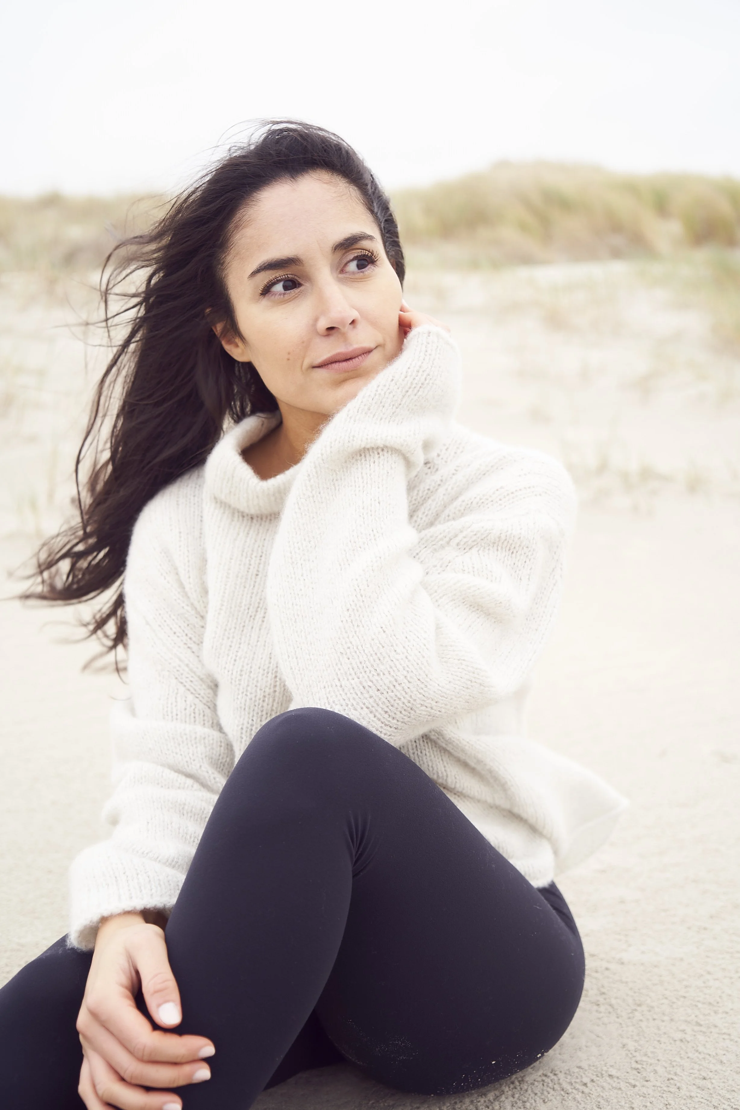 Frau in weißem Pullover sitzt nachdenklich am Strand