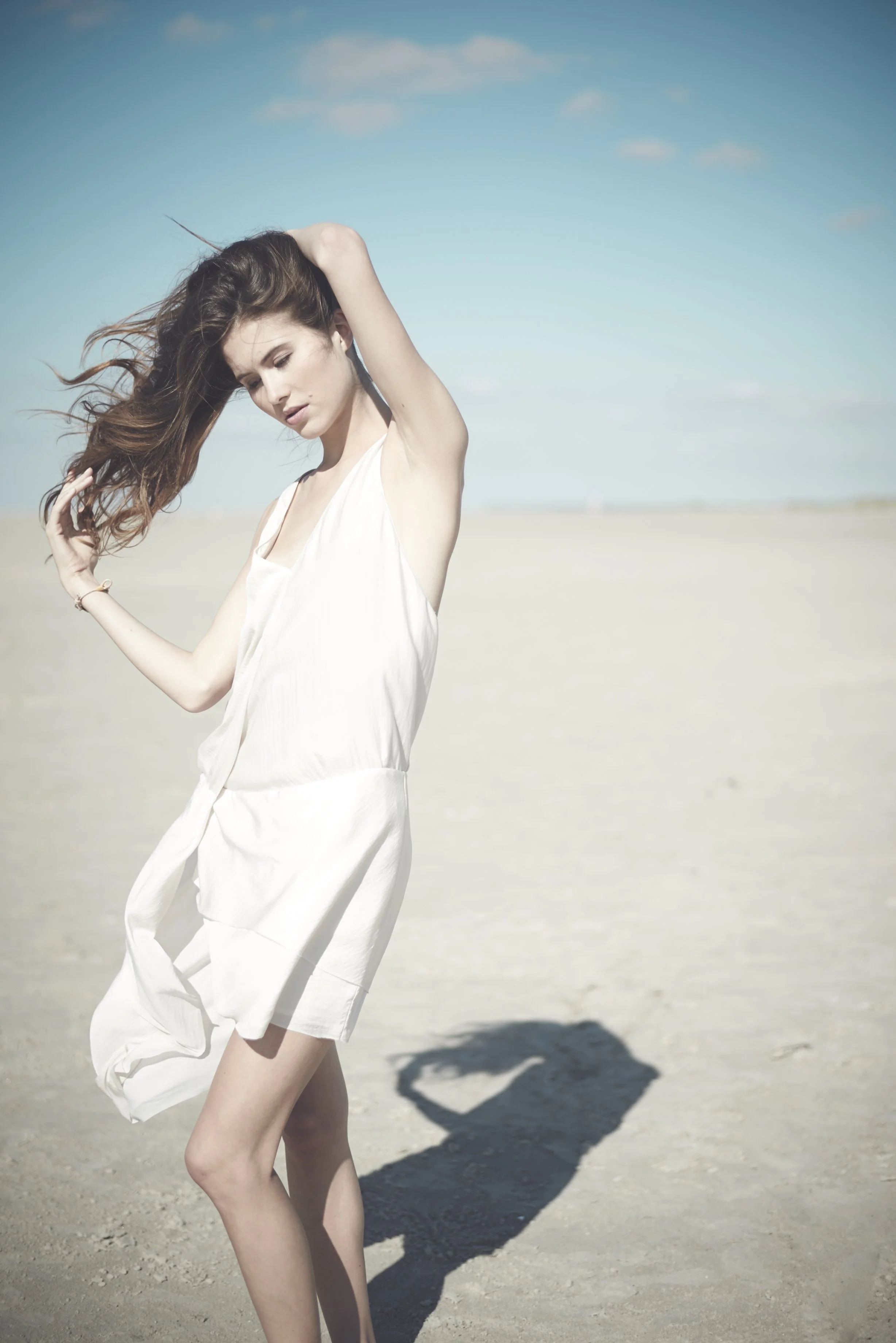 Ein Modefoto einer jungen Frau die sich am Strand in ihr Haar fässt