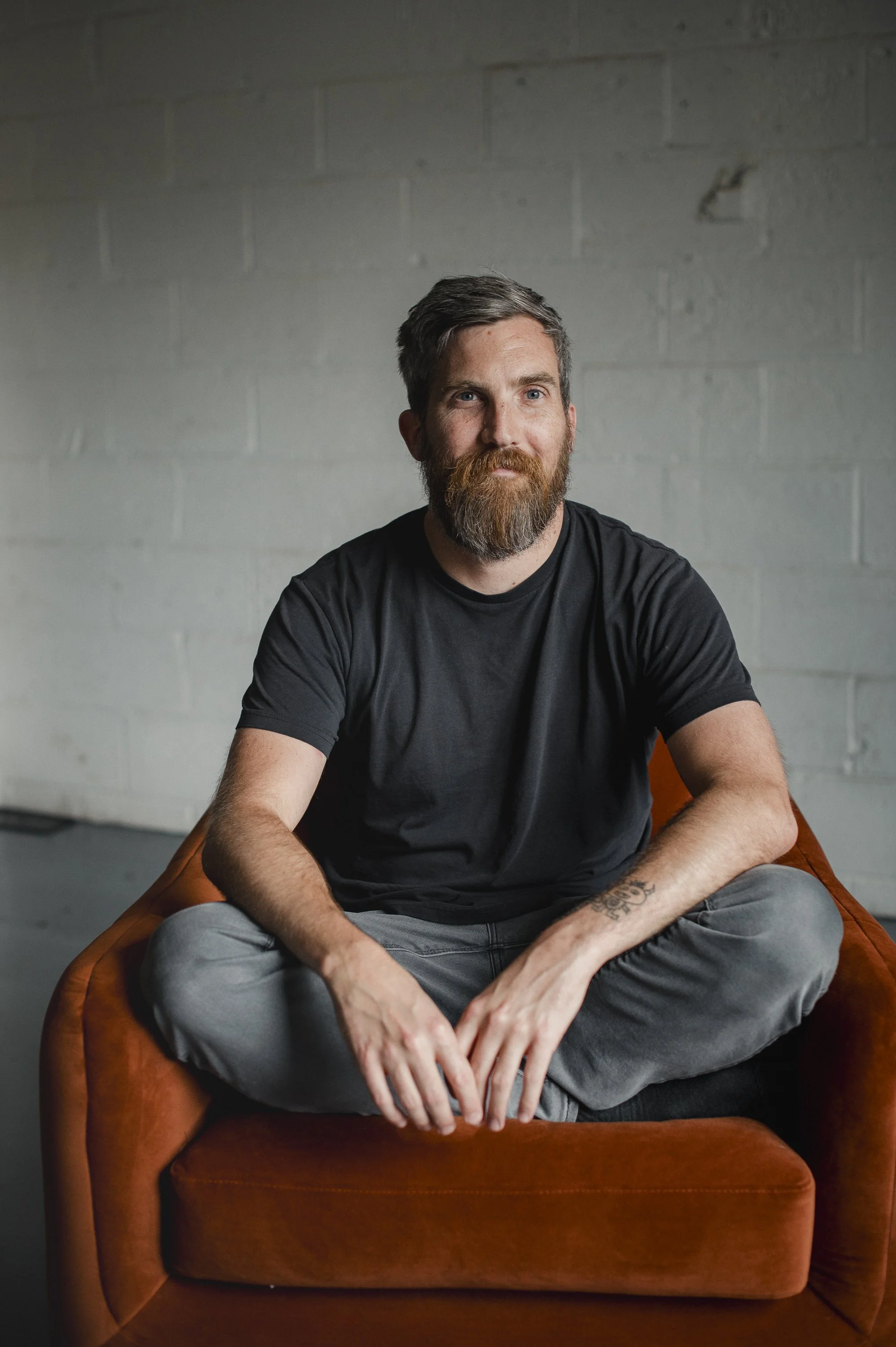 Man with a beard sitting cross-legged on an orange chair