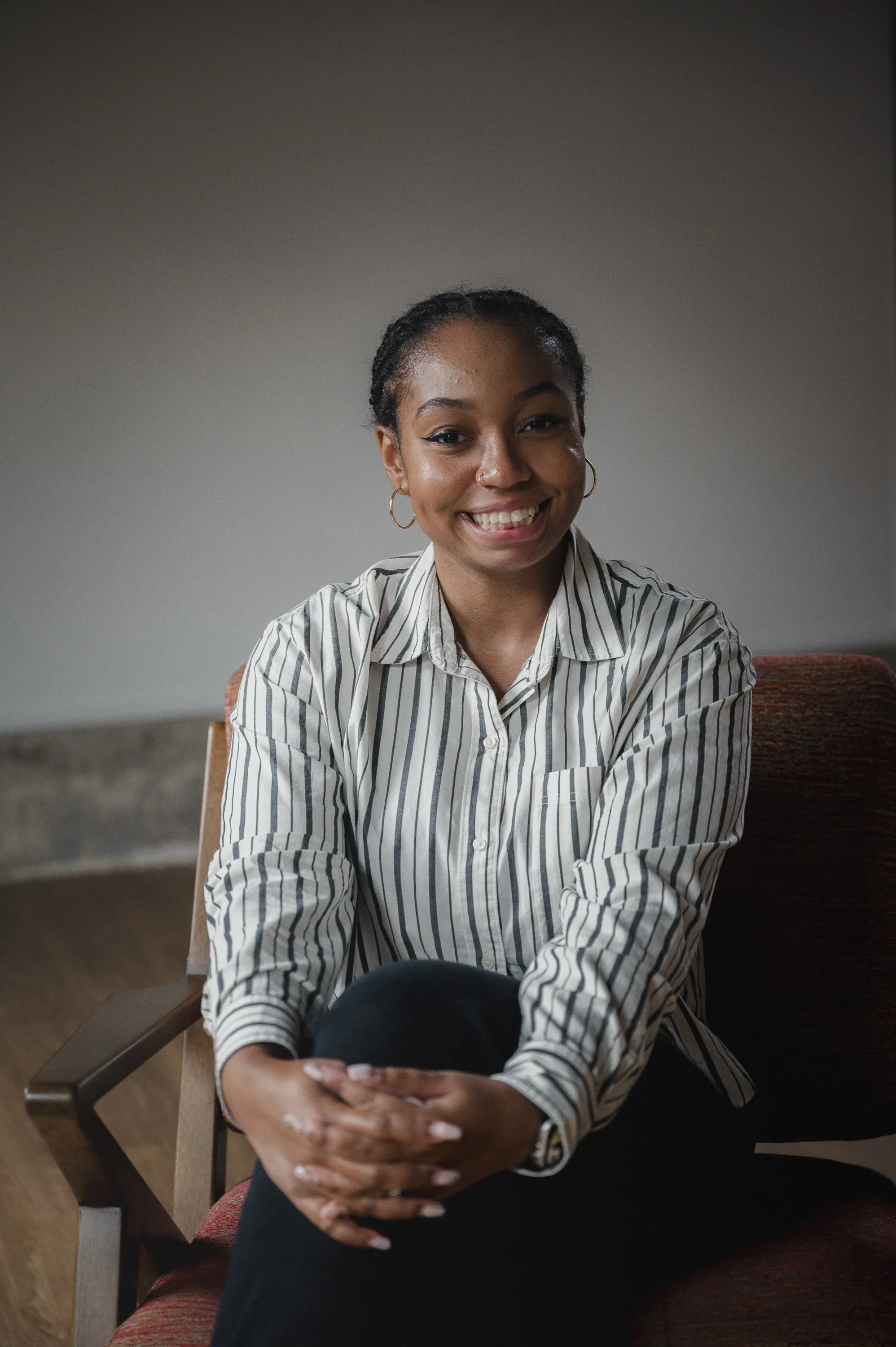 Smiling person sitting on a chair wearing a striped shirt.