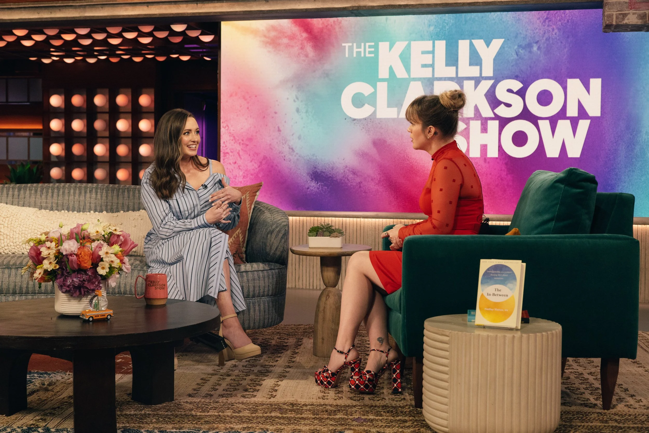 Two women engaged in conversation on a talk show set with a colorful backdrop and