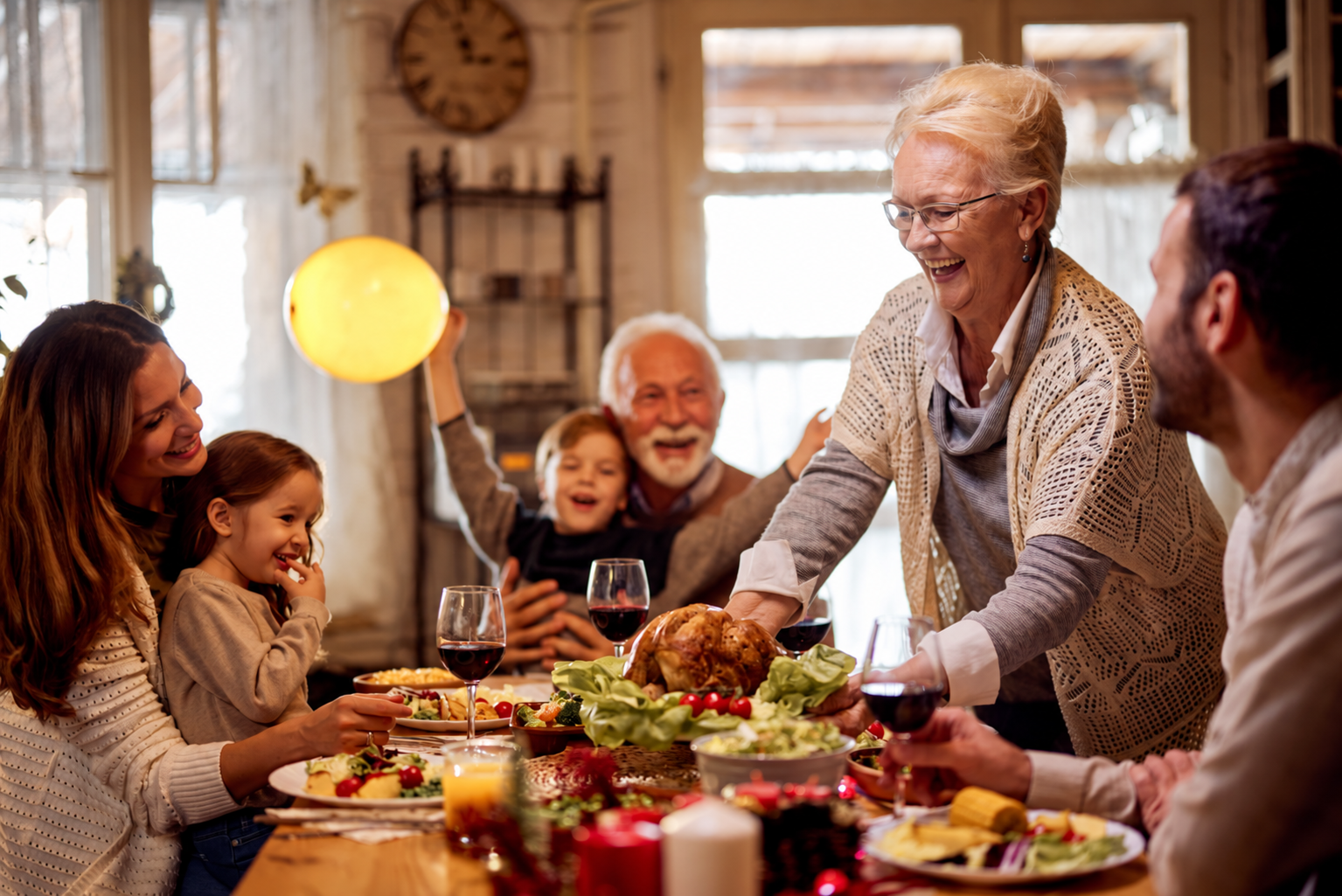 Family gathered around a dinner table celebrating Thanksgiving, with a roasted turkey, salads, and glasses of red wine.