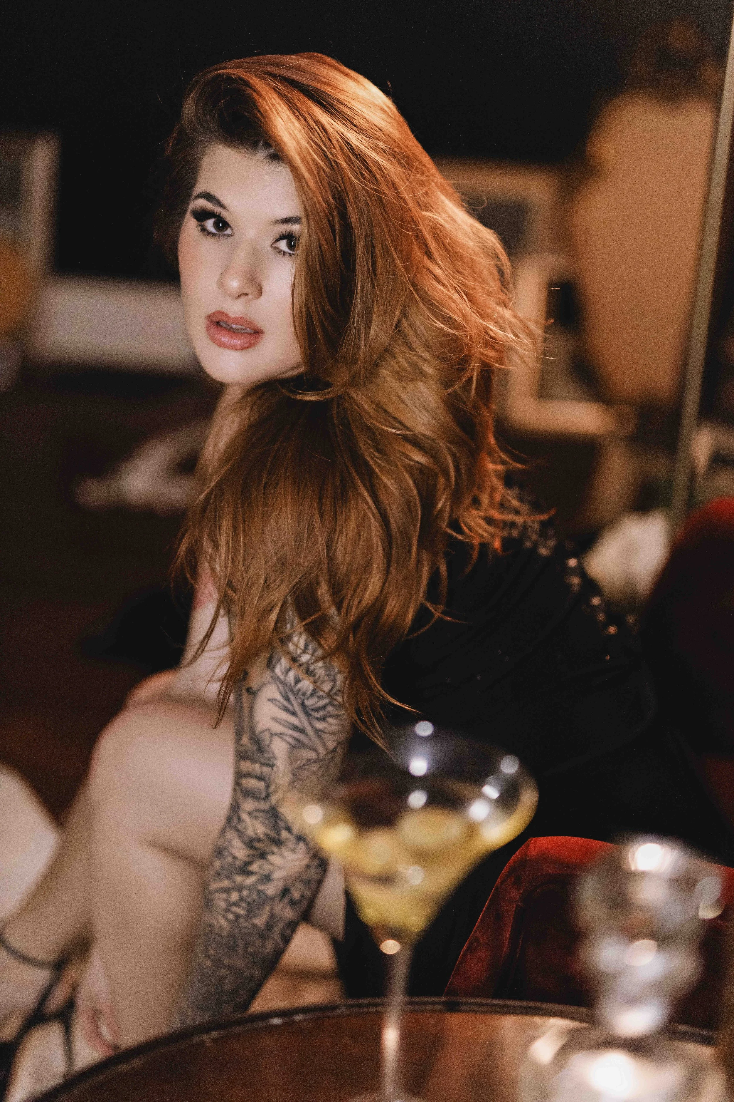 WOMAN WITH TATTOOS TOUCHING HER LEG AND A MARTINI GLASS IN THE FOREGROUND