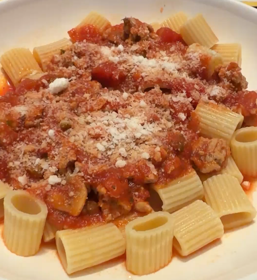 Plate of cooked rigatoni pasta with meat sauce topped with grated cheese.
