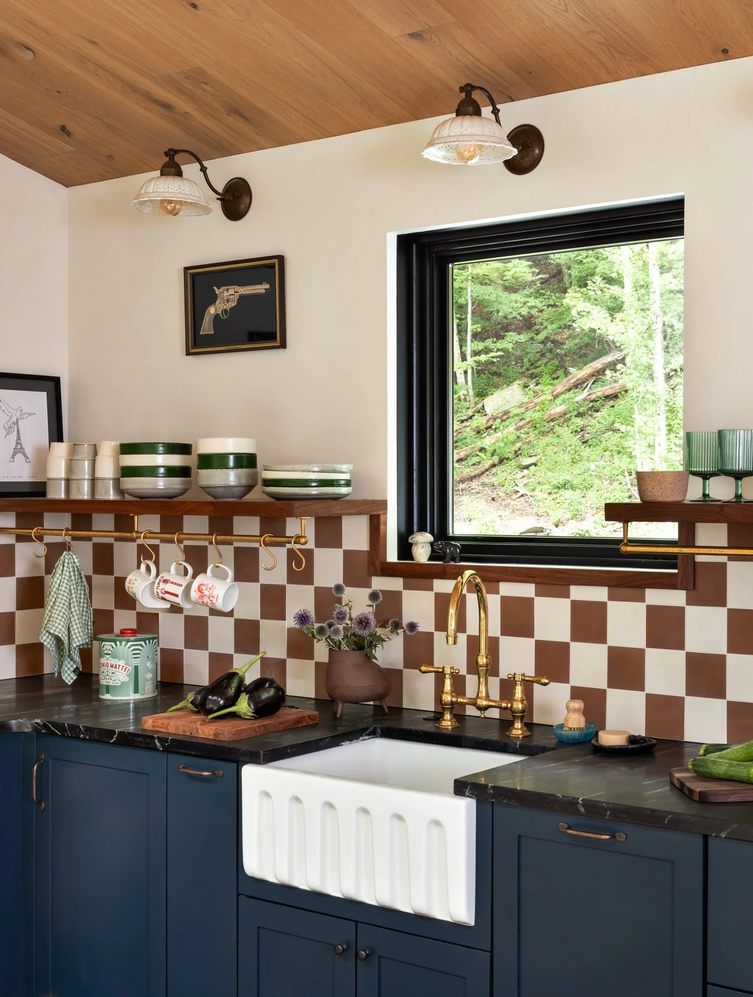 Blue cabinets, a burgundy-and-cream checkerboard backsplash, brass faucet, farmhouse sink, and open wood shelves.
