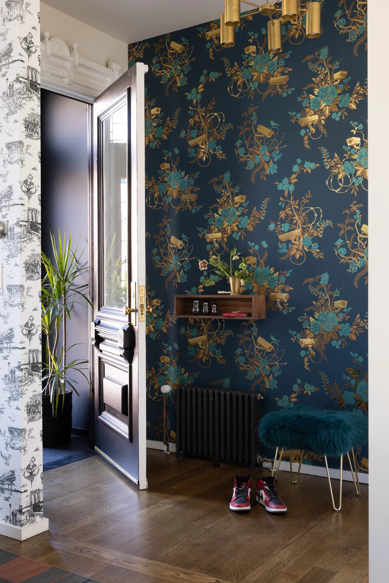 Hallway with dark floral wallpaper, contrasting white patterned wall, black radiator, and wood flooring.