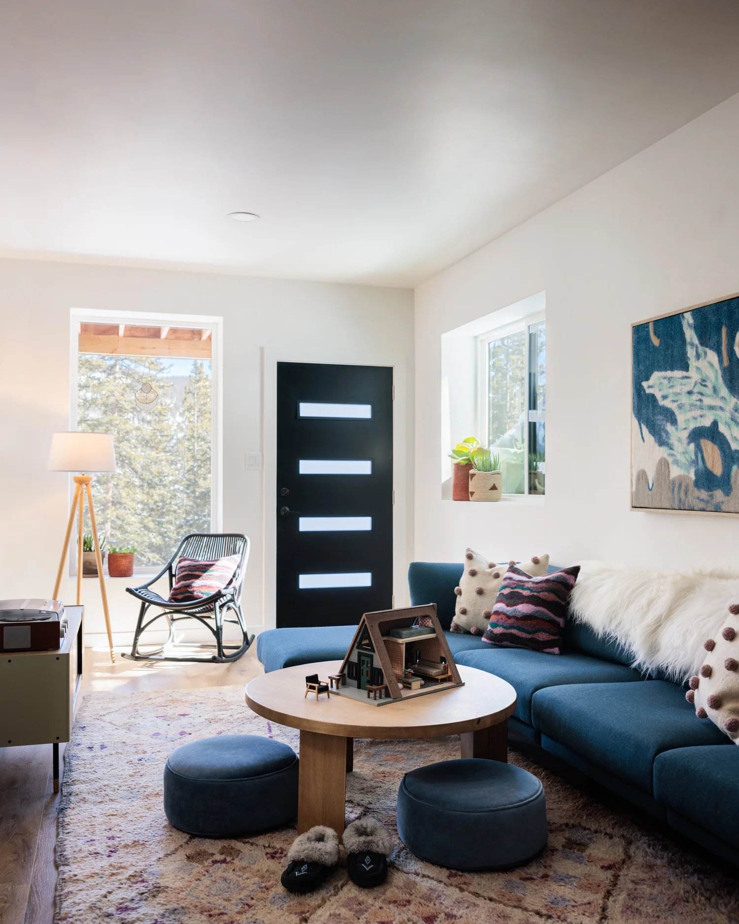 Living room with blue sectional, round wood coffee table, blue ottomans, patterned rug, and abstract art.