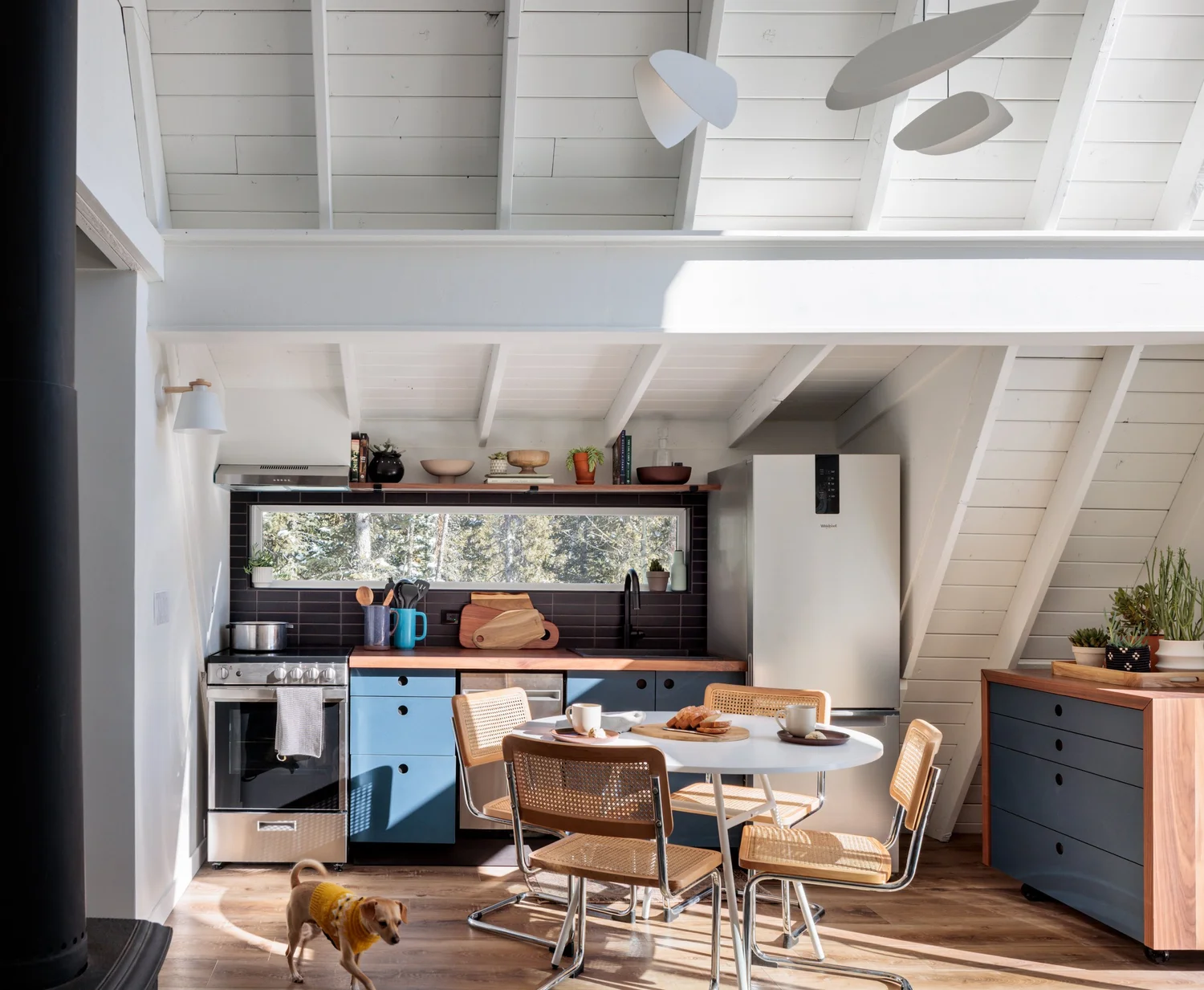 Camp Altezza kitchen and dining area with blue cabinets, wood counters, window backsplash, and white exposed ceiling beams.