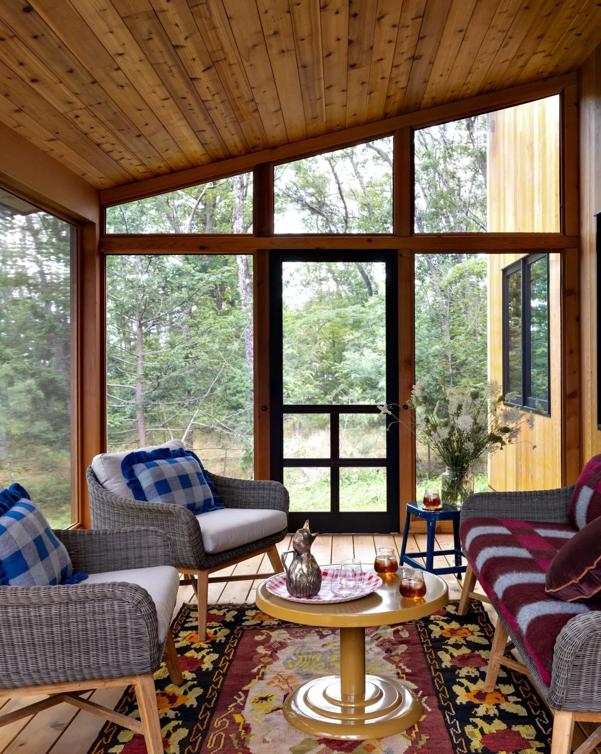 Screened porch with wood ceiling, patterned seating, woven chairs, and woodland views.