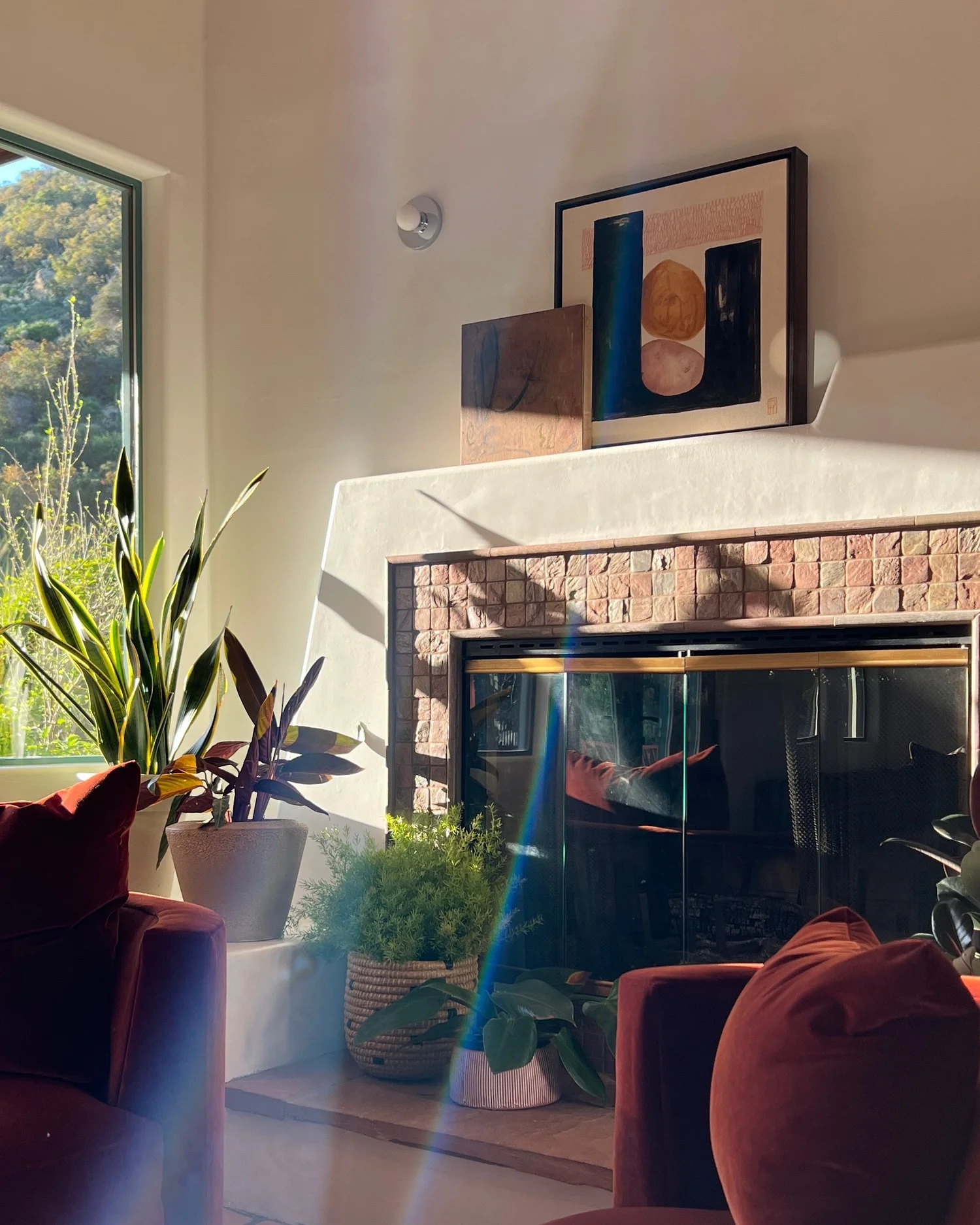 Danielle Hutchens artwork above a brick fireplace, with burgundy velvet seating and indoor plants.