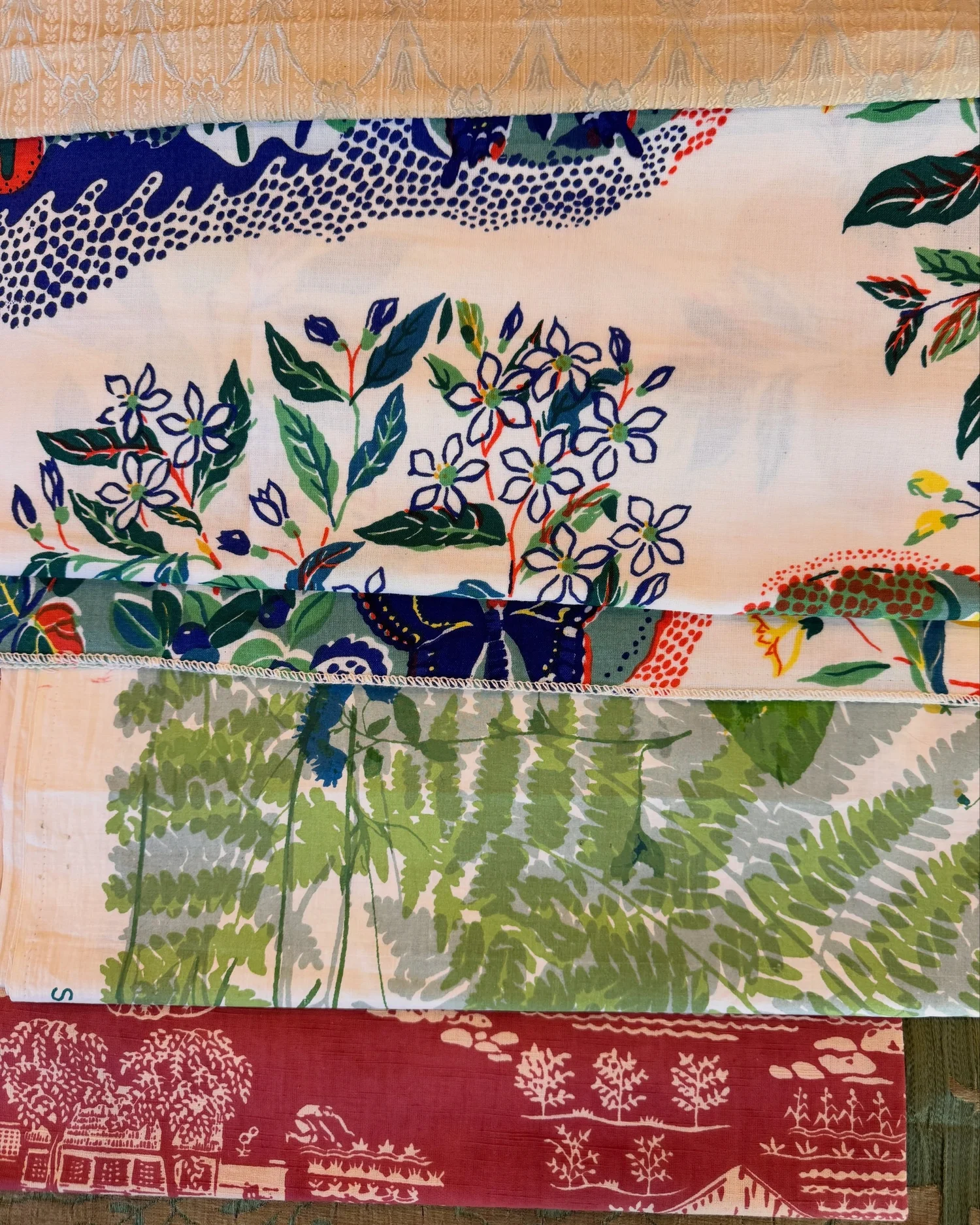 Vintage textile samples with floral embroidery, blue trim, green foliage, and red patterned fabric.