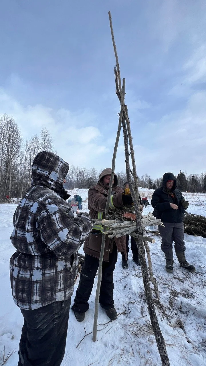 People outdoors in winter working on a signal fire made of sticks and branches.