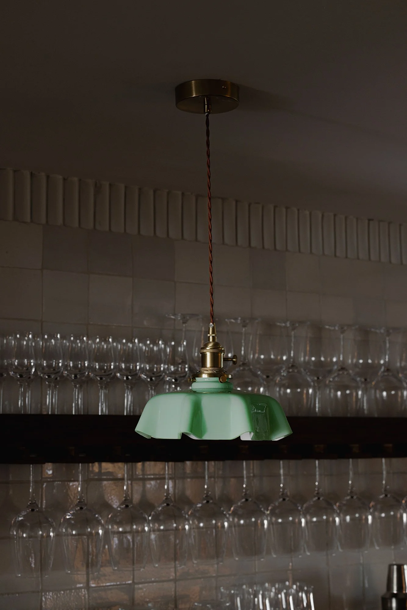 Close-up of a scalloped green pendant light with brass hardware, suspended above glassware at The Lamb restaurant in Mexico City.