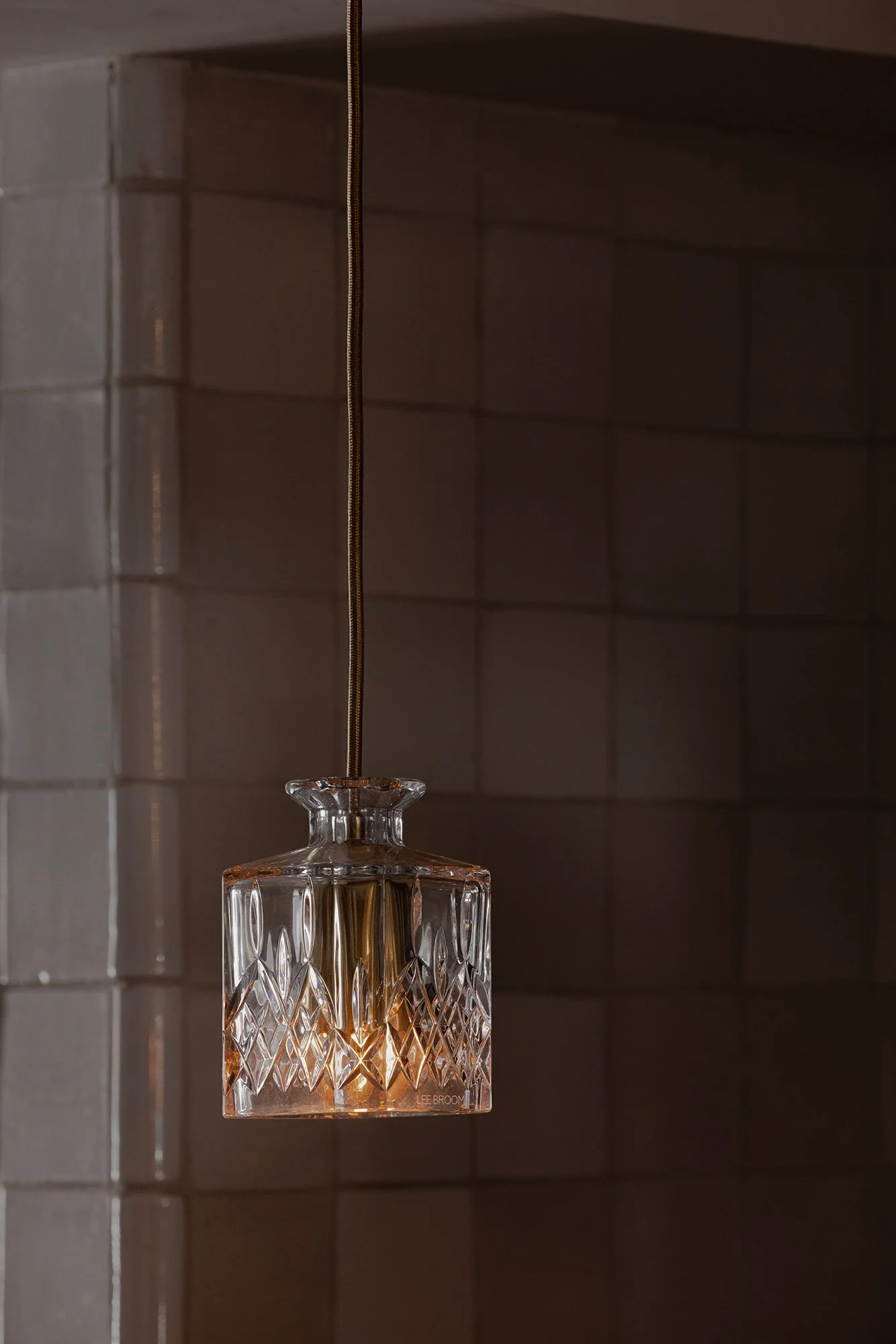 Detail of a crystal decanter pendant light by Lee Broom, glowing warmly against hand-glazed white tile at The Lamb restaurant.
