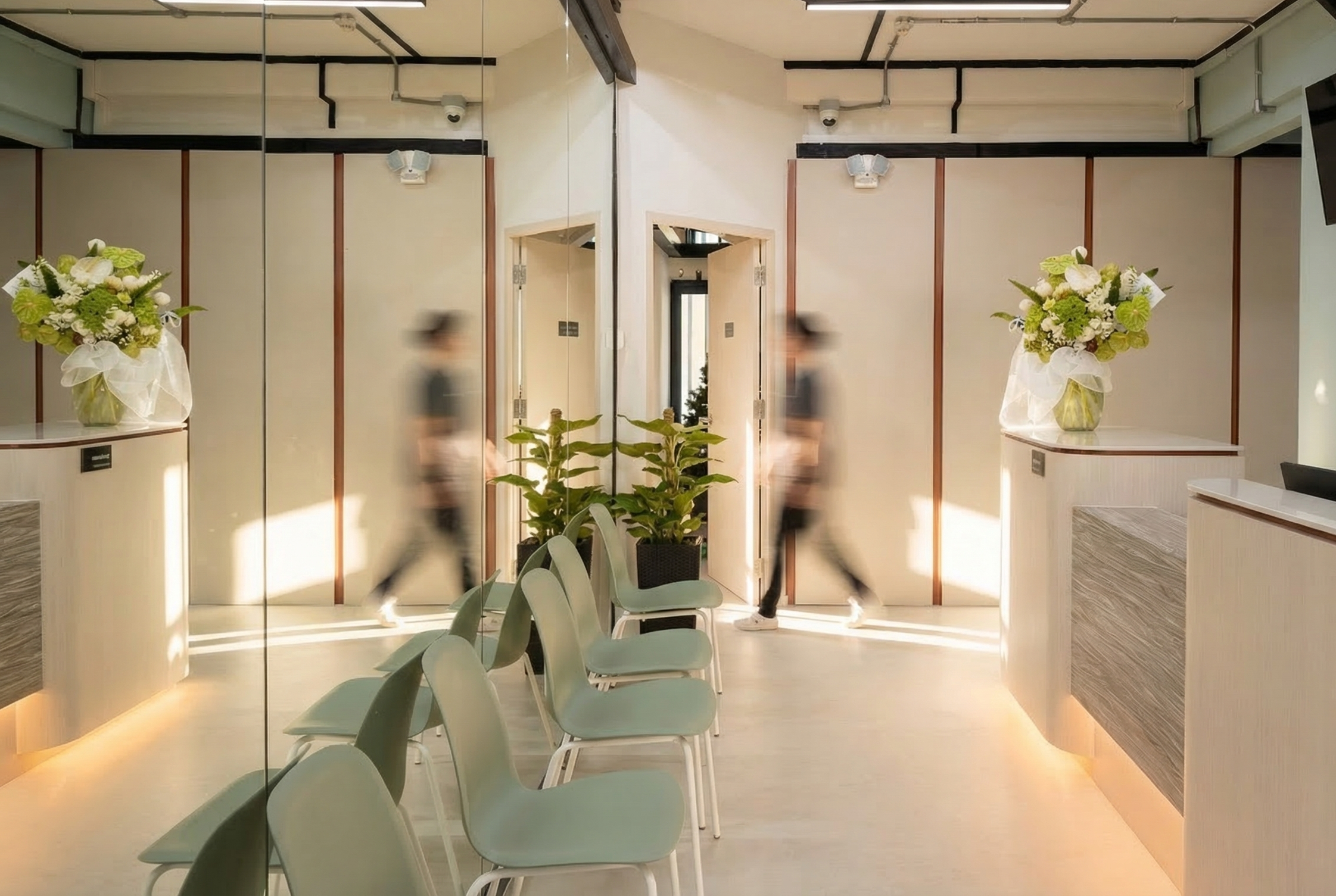 Modern reception area with a mirrored wall, seating, potted plants, and floral arrangements in vases.