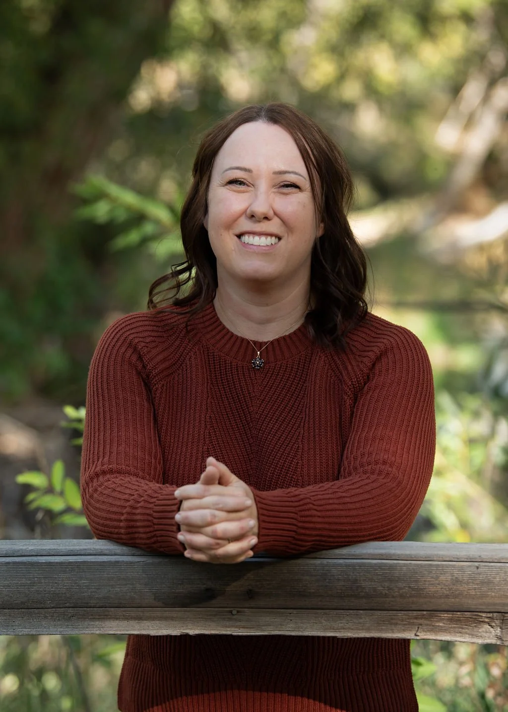 Wellness coach Sarah Henry smiling outdoors, leaning on a wooden fence.