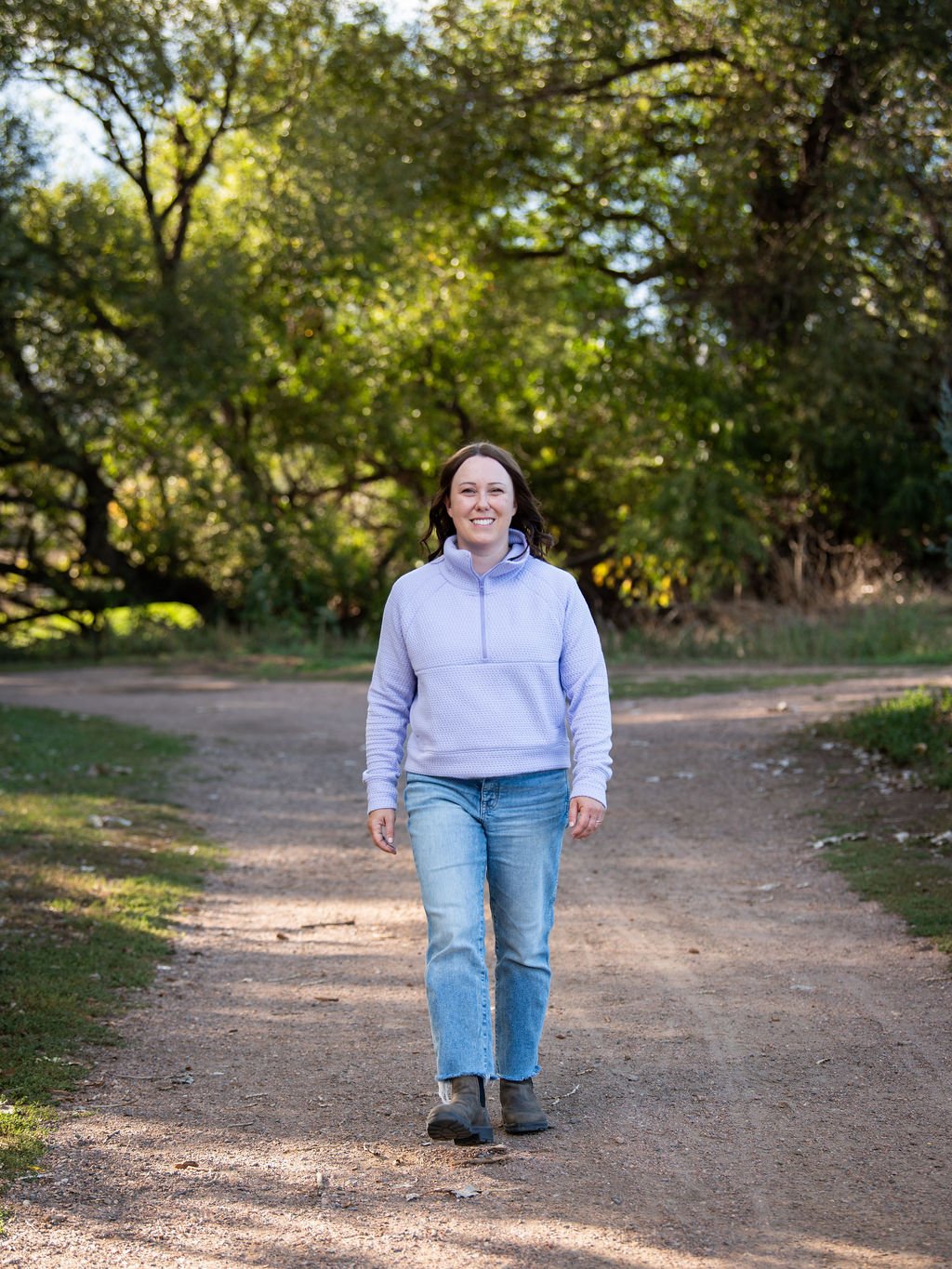 Sarah Henry walking along a wooded trail in a lilac pullover, surrounded by trees.
