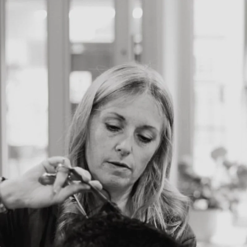 A woman with blonde hair doing someone's hair or makeup in a bright indoor space.
