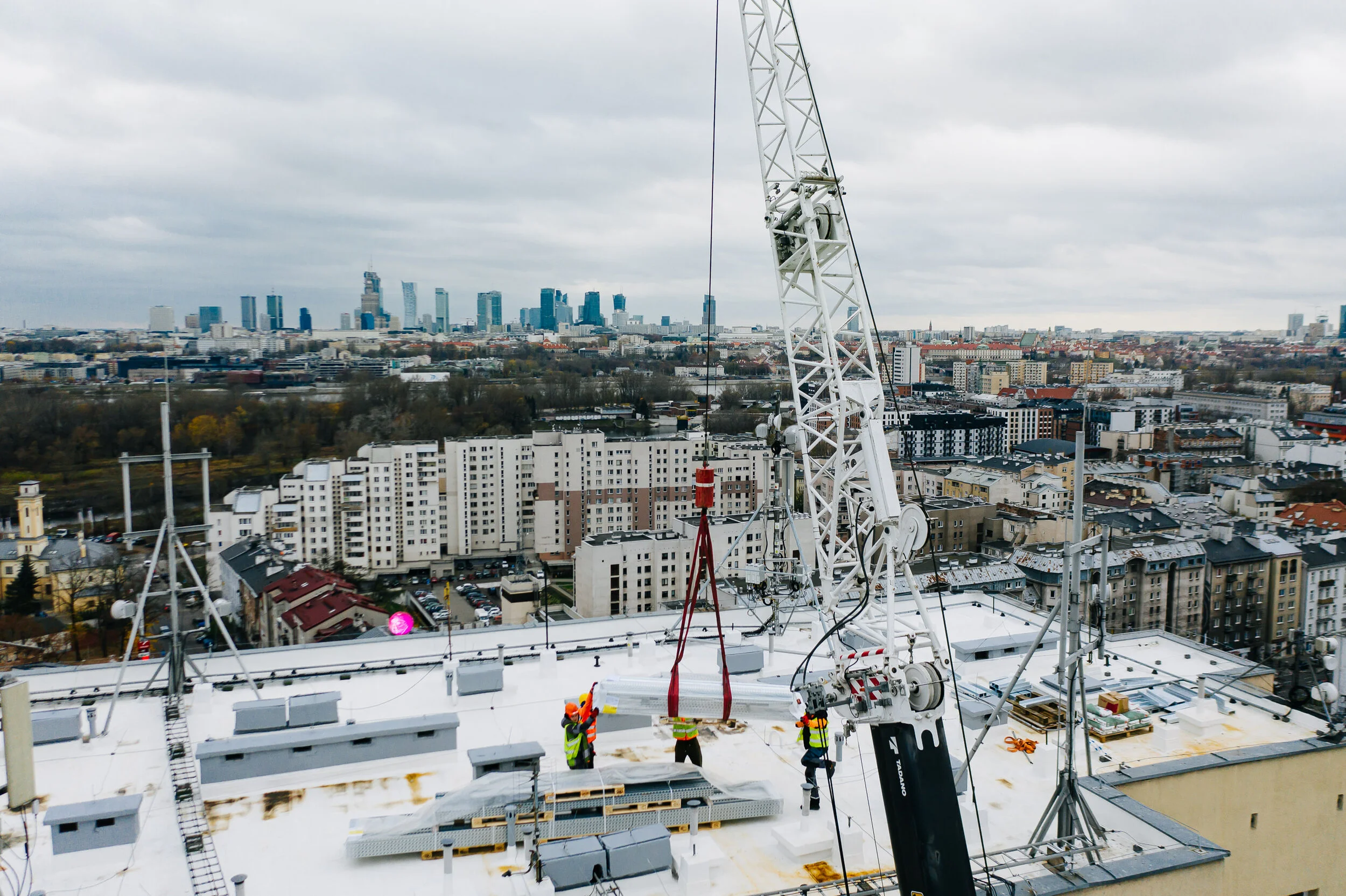Construction workers on a rooftop working with a crane on a building in an urban area with a city skyline in the background.