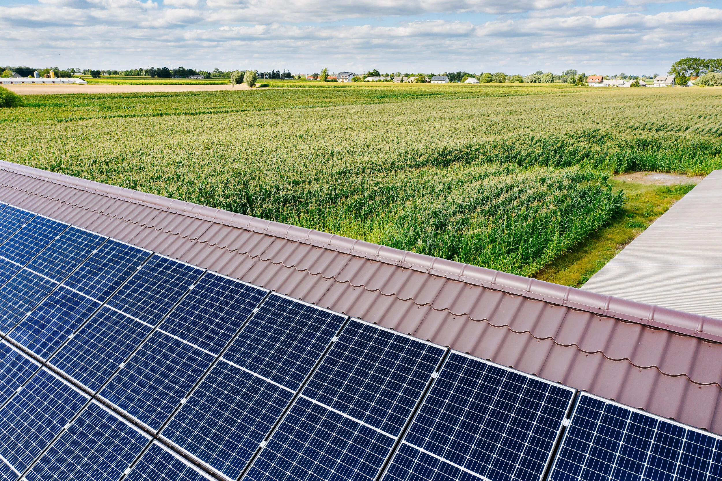 Solar panels on a roof overlooking a green farmland and a partly cloudy sky.