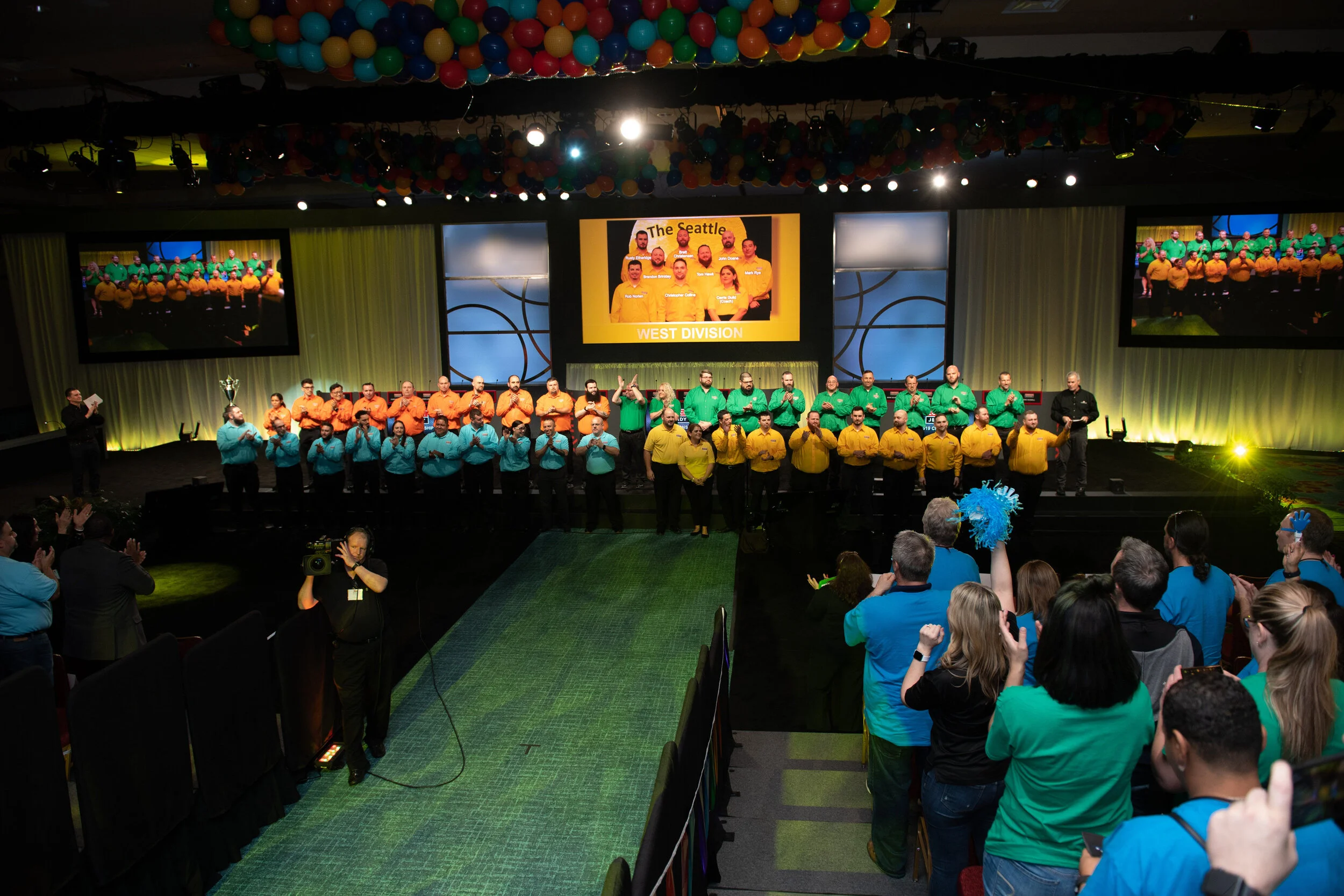 Event stage with four teams of contestants in brightly colored shirts