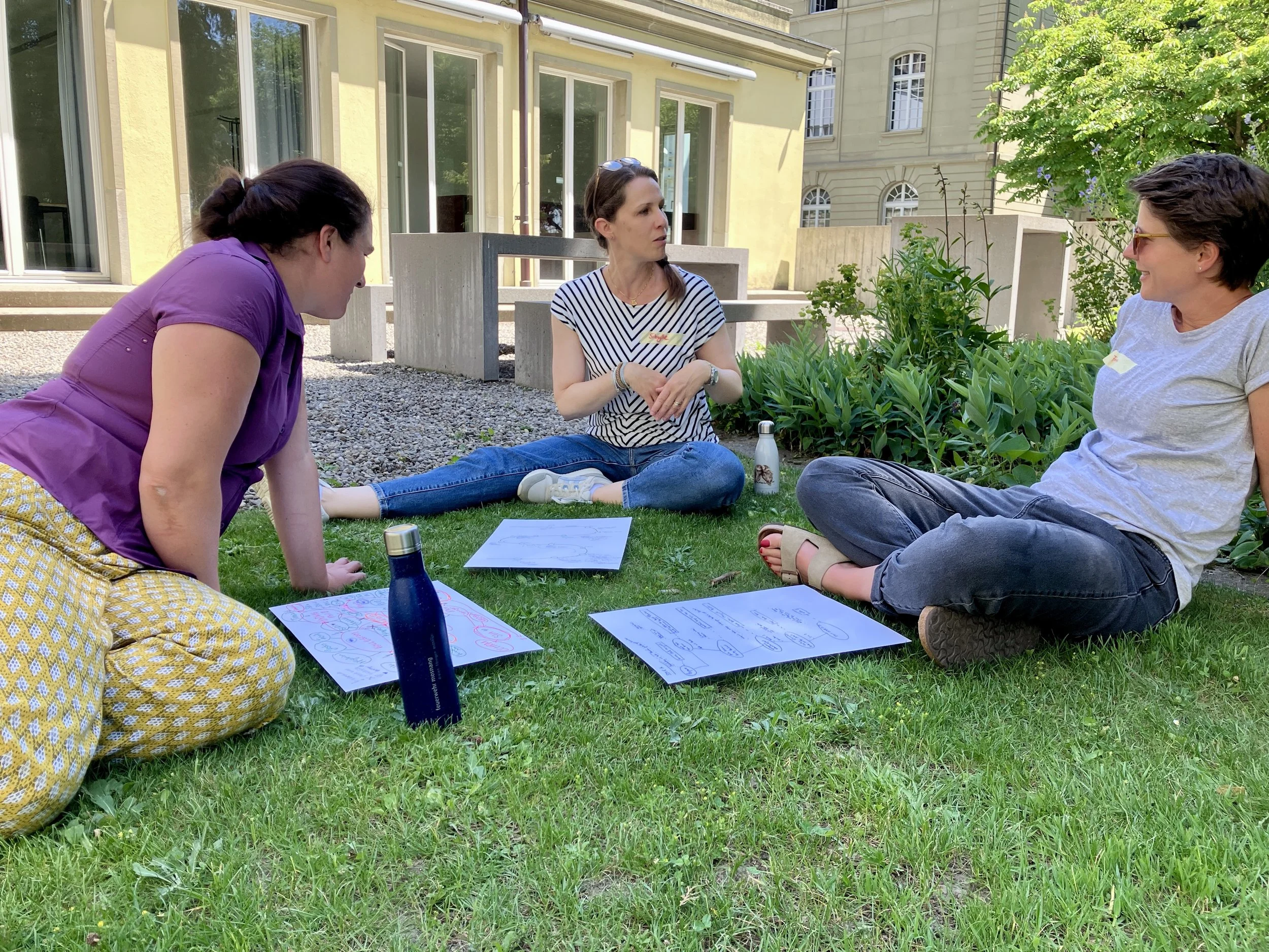 Drei Personen besprechen im Gras sitzend