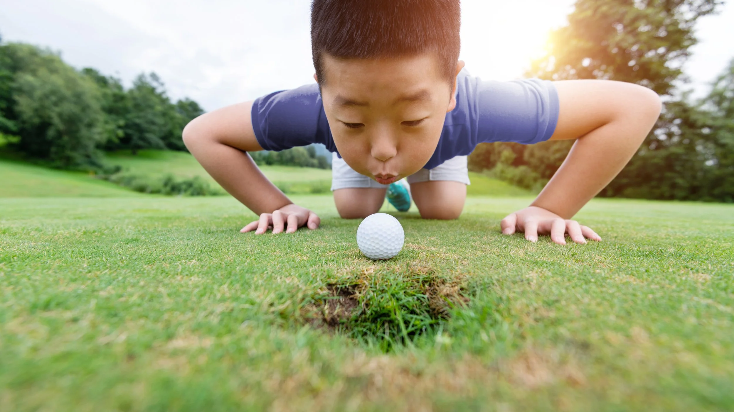 Boy blowing golf ball to hole_504164908_ClrAdj.jpg