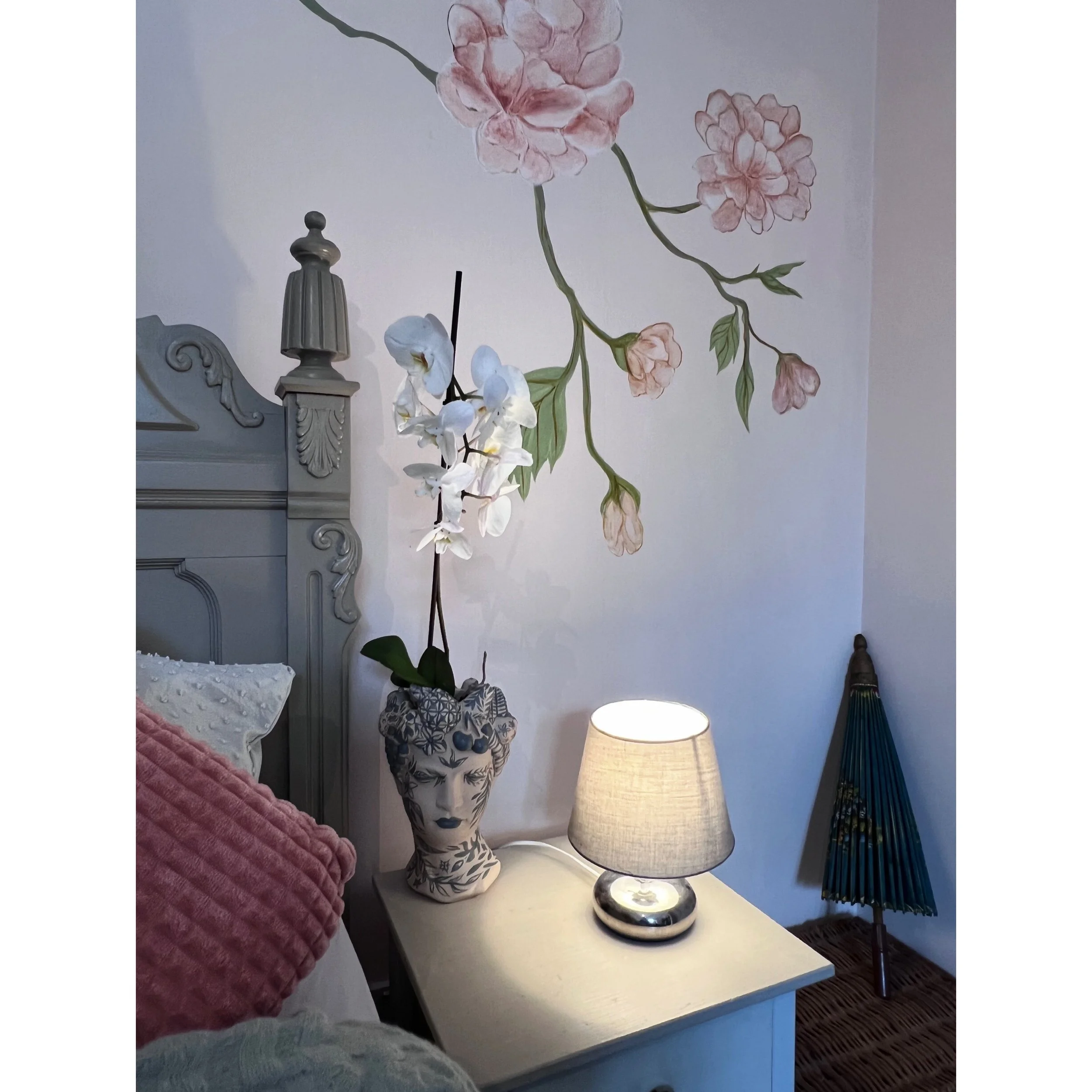 Decorative living room wall with a large blue and black mural of a woman's face with red lips, surrounded by photographs, a plant, and modern furniture.
