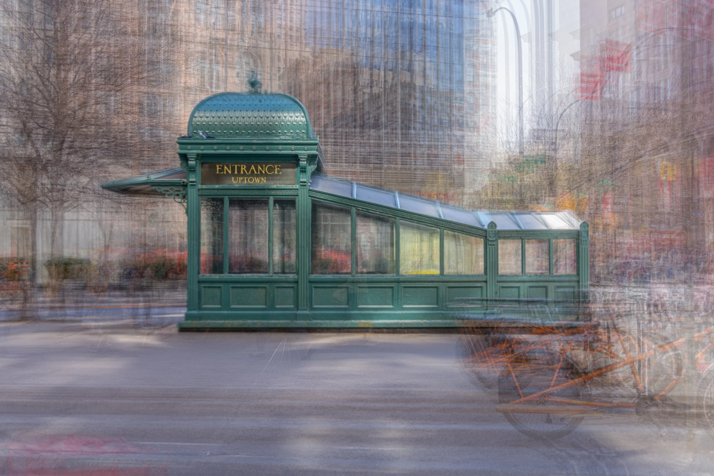 A green glass covered subway entrance with a sign that reads "ENTRANCE UPTOWN". The background shows a cityscape with buildings and trees, and a street with motion-blurred cars.  Astor Place New York