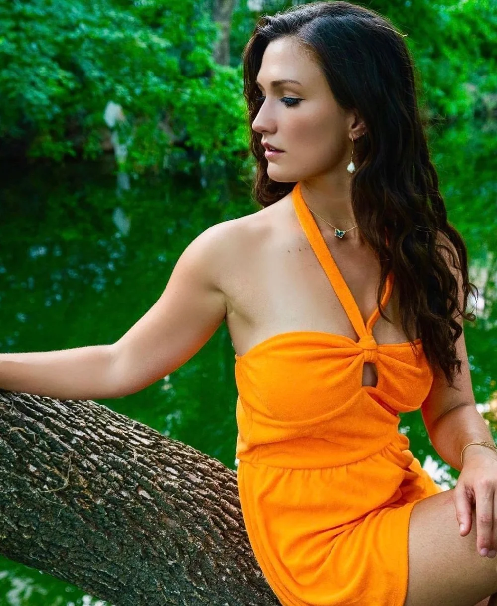 Stephanie in orange dress sitting on a tree branch by water