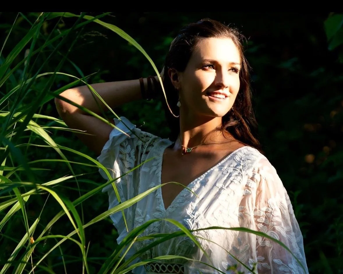 Stephanie in white embroidered blouse among tall grass in sunlight