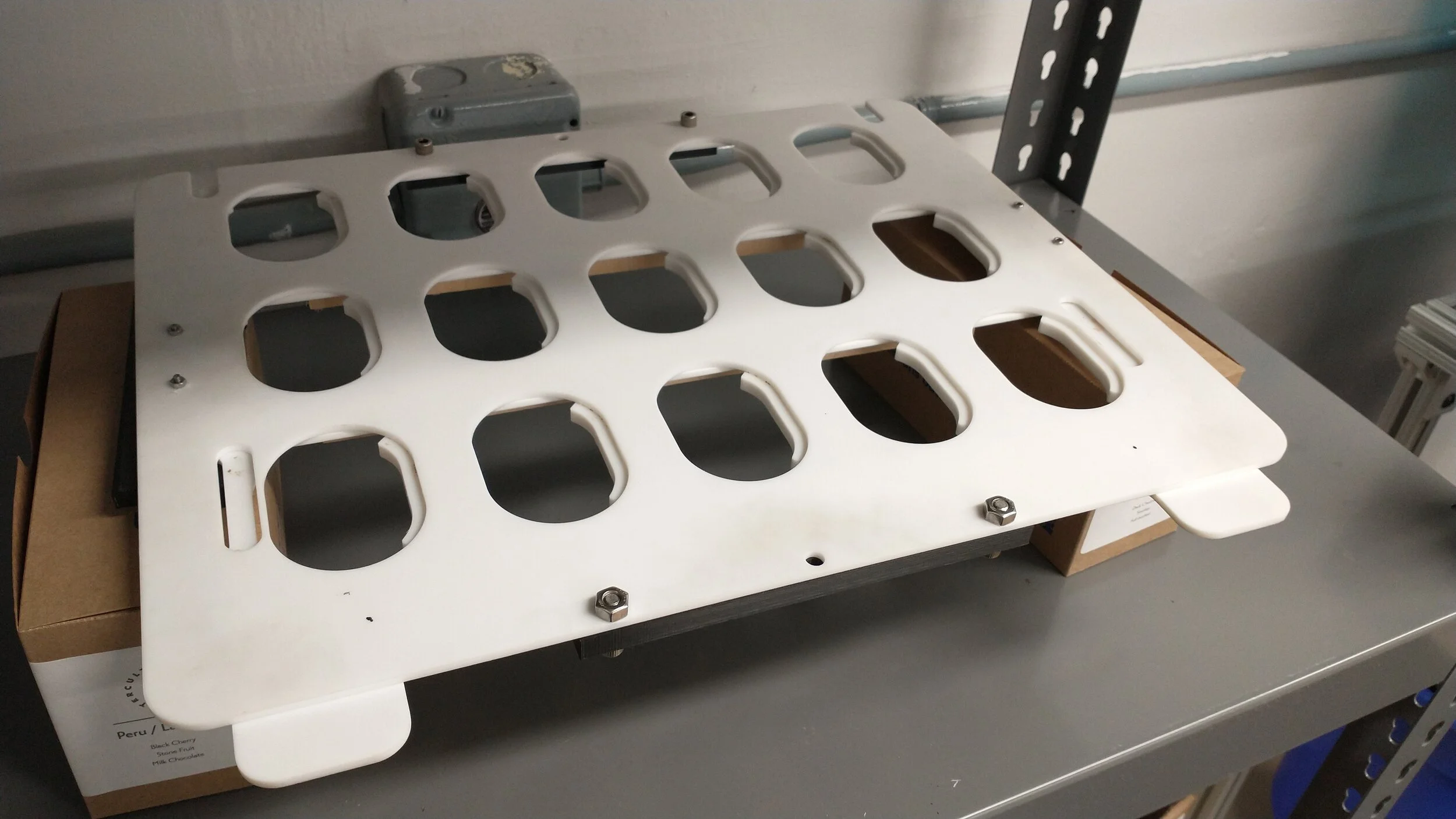 A view of the open position of the removable tray. The front tabs are connected to a plate that moves the supports on the left side of the holes. When the tabs are moved, the supports move with them, allowing the simultaneous release of all 15 pods i