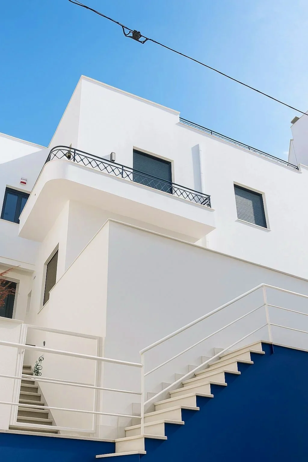 Modern white building with balconies and stairs, against a clear blue sky.