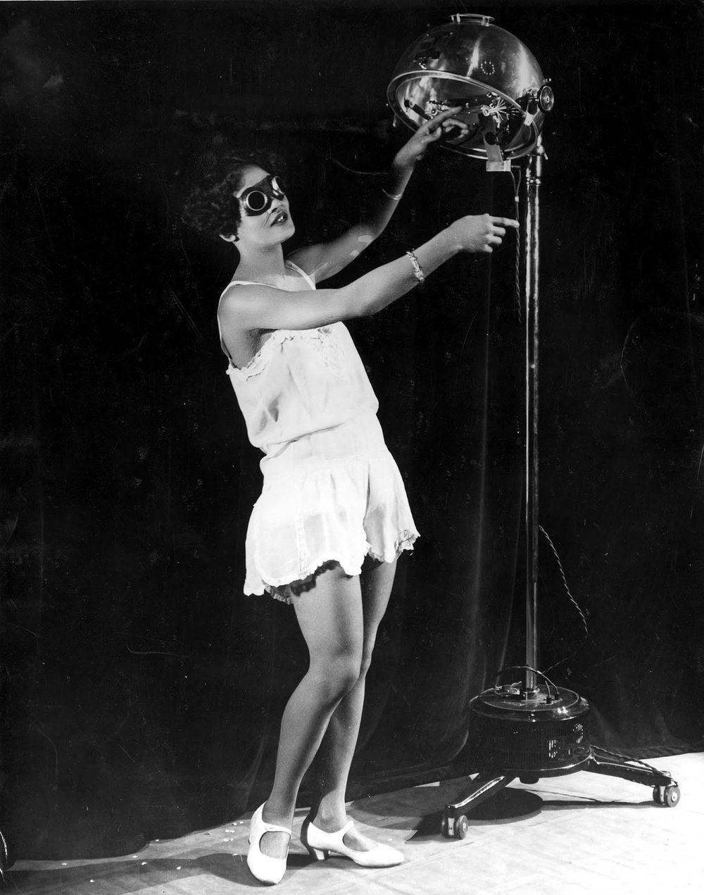  23 year old Alma Smith, the ‘cleverest soubrette’ of the cast of ‘Blackbirds’ at the London Pavilion, receiving her daily dose of ultra violet rays from a sun machine. 1929. 