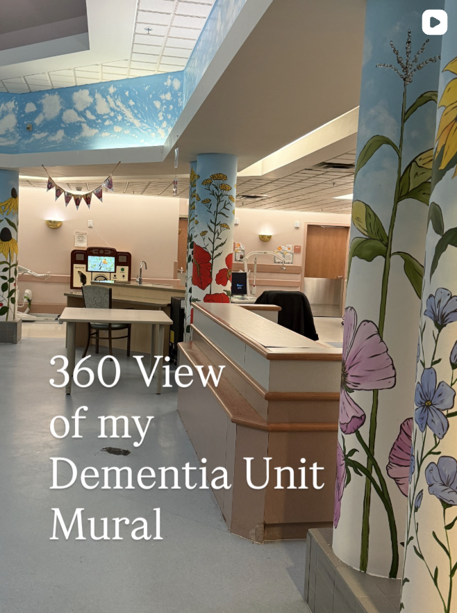 Interior view of a dementia unit with colorful floral and nature murals on the walls and pillars, featuring a reception desk and a small play area with a computer.