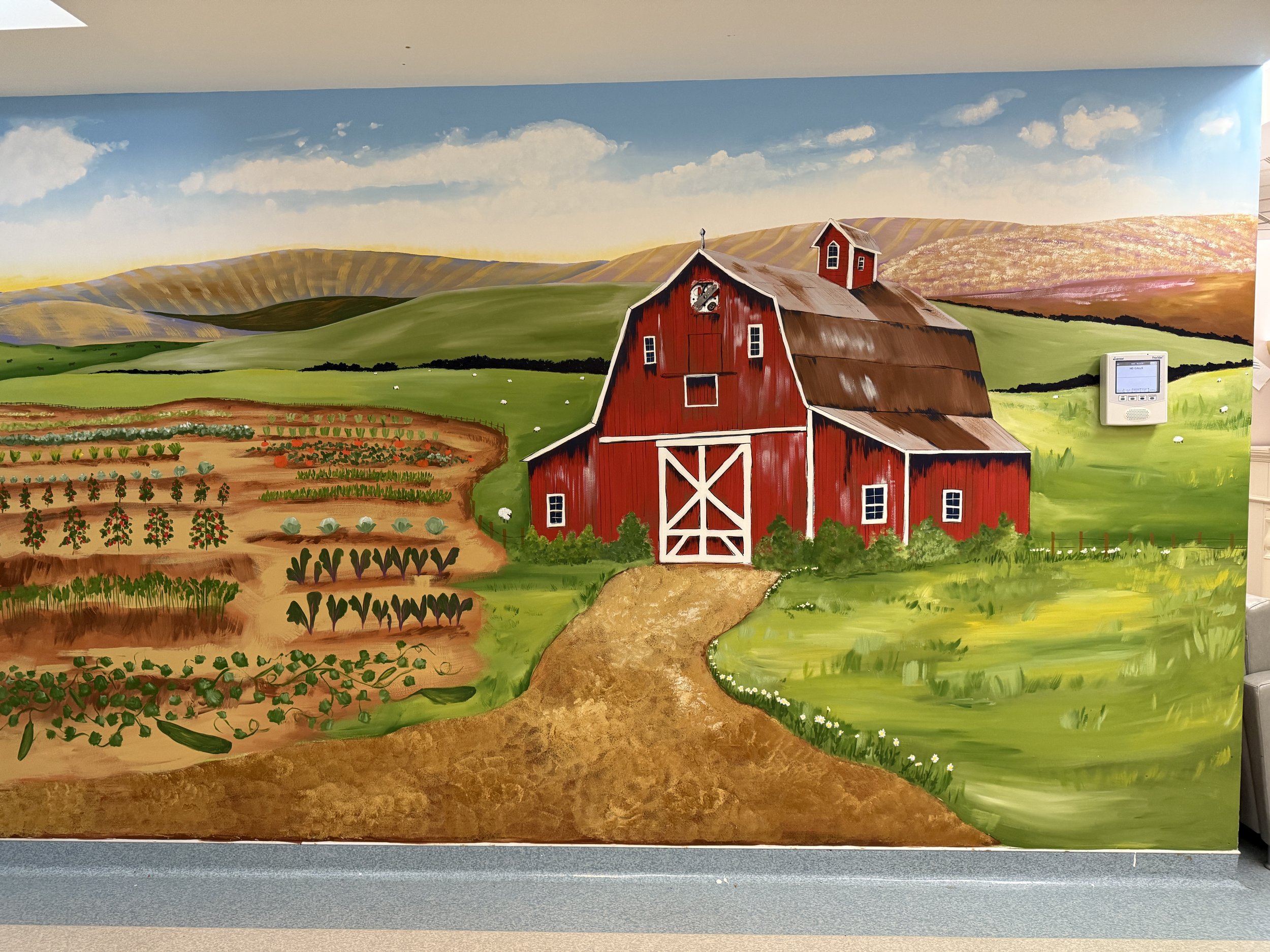 A colorful mural painting of a farm scene with a red barn, green fields, and distant mountains in the background, on an interior wall.