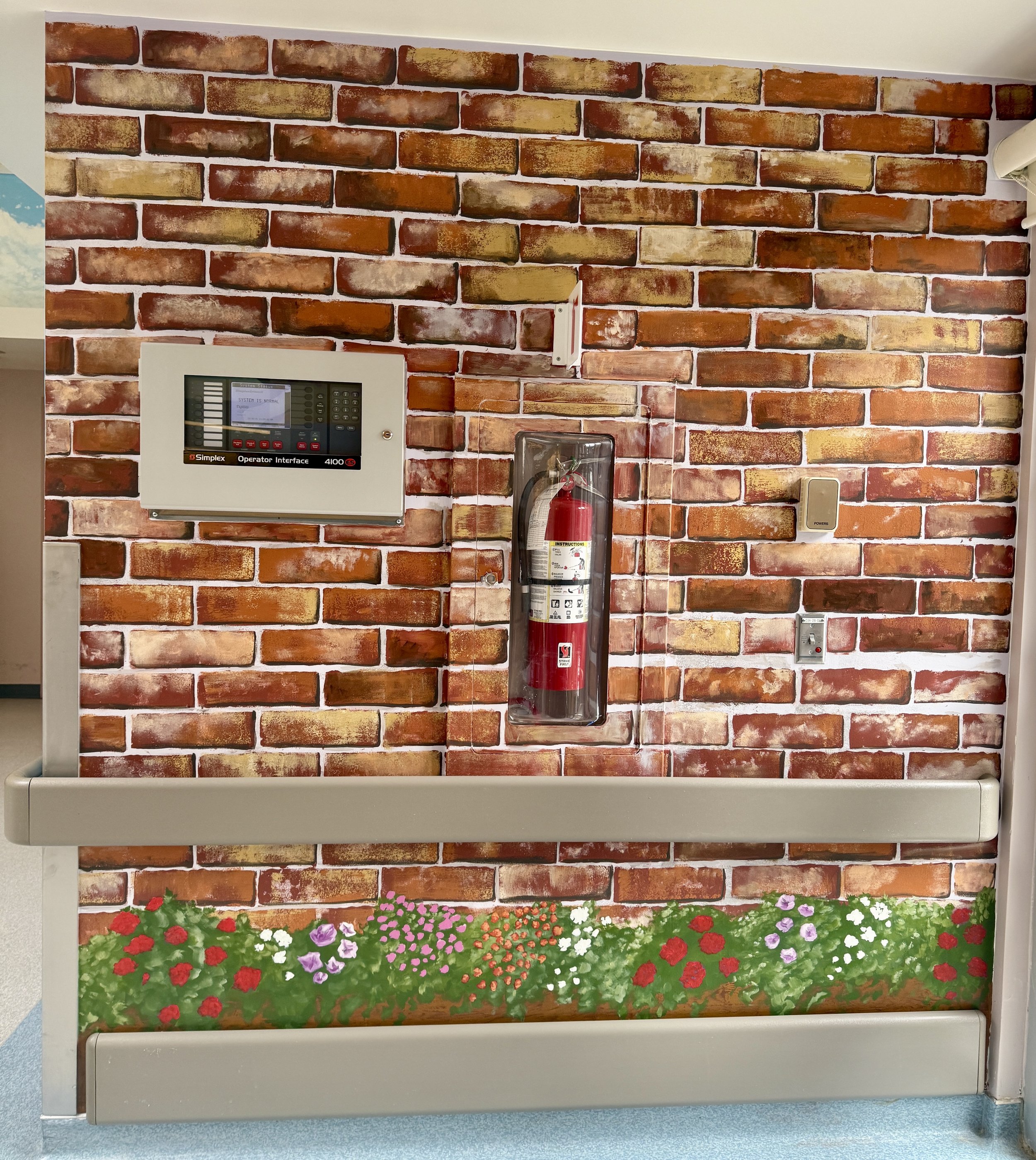 Brick wall with fire extinguisher, fire alarm, control panel, and flower mural at the bottom.