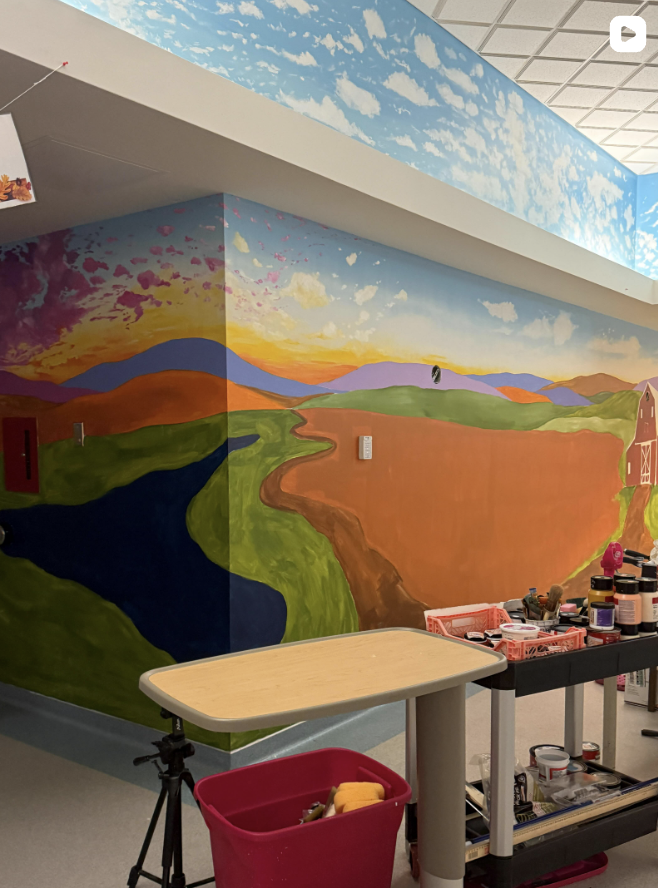 Mural of a colorful landscape with a winding river, hills, and a sky with clouds, painted on the walls and ceiling of a room.