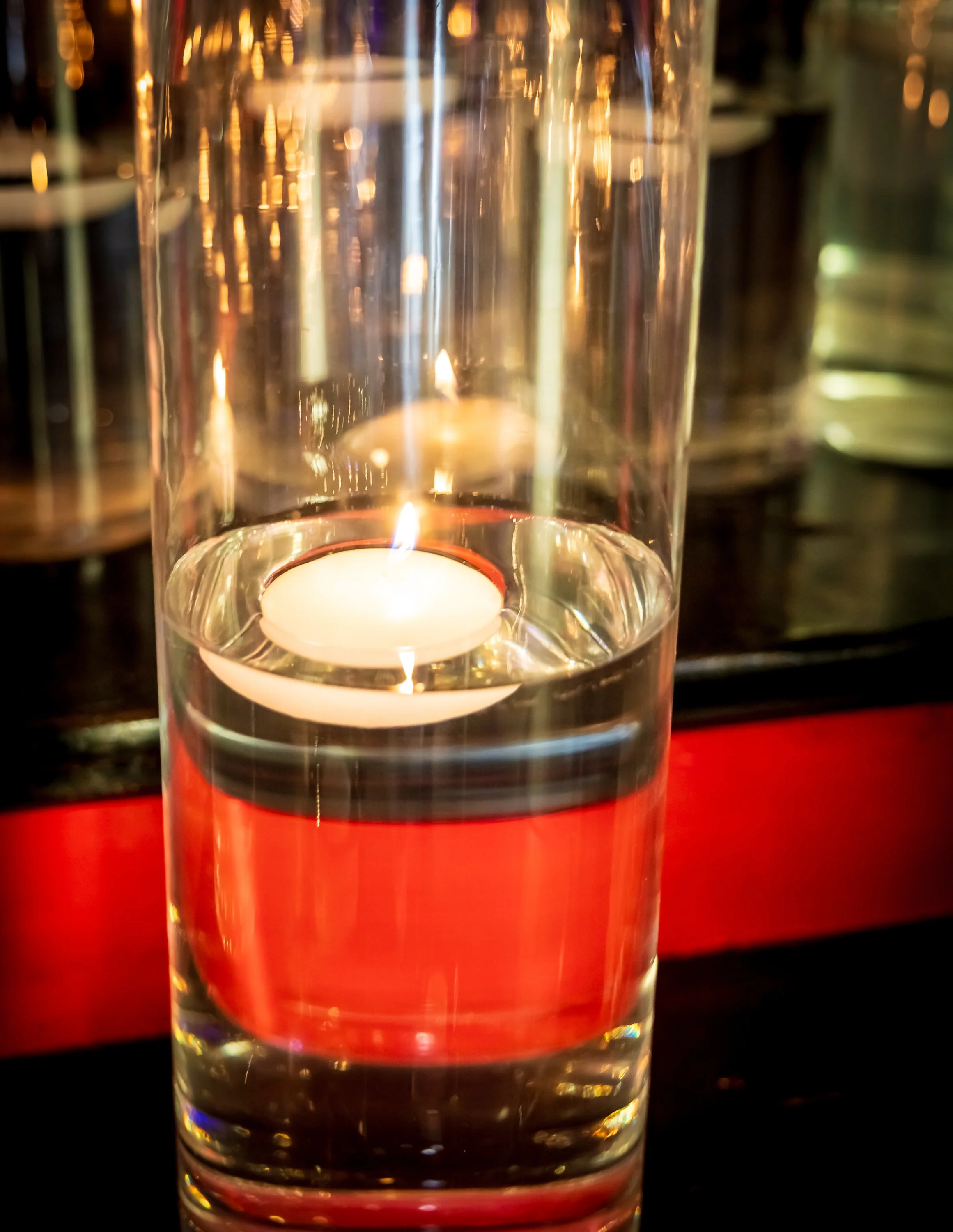 A floating tealight candle in a glass of water with reflections and a blurred background.