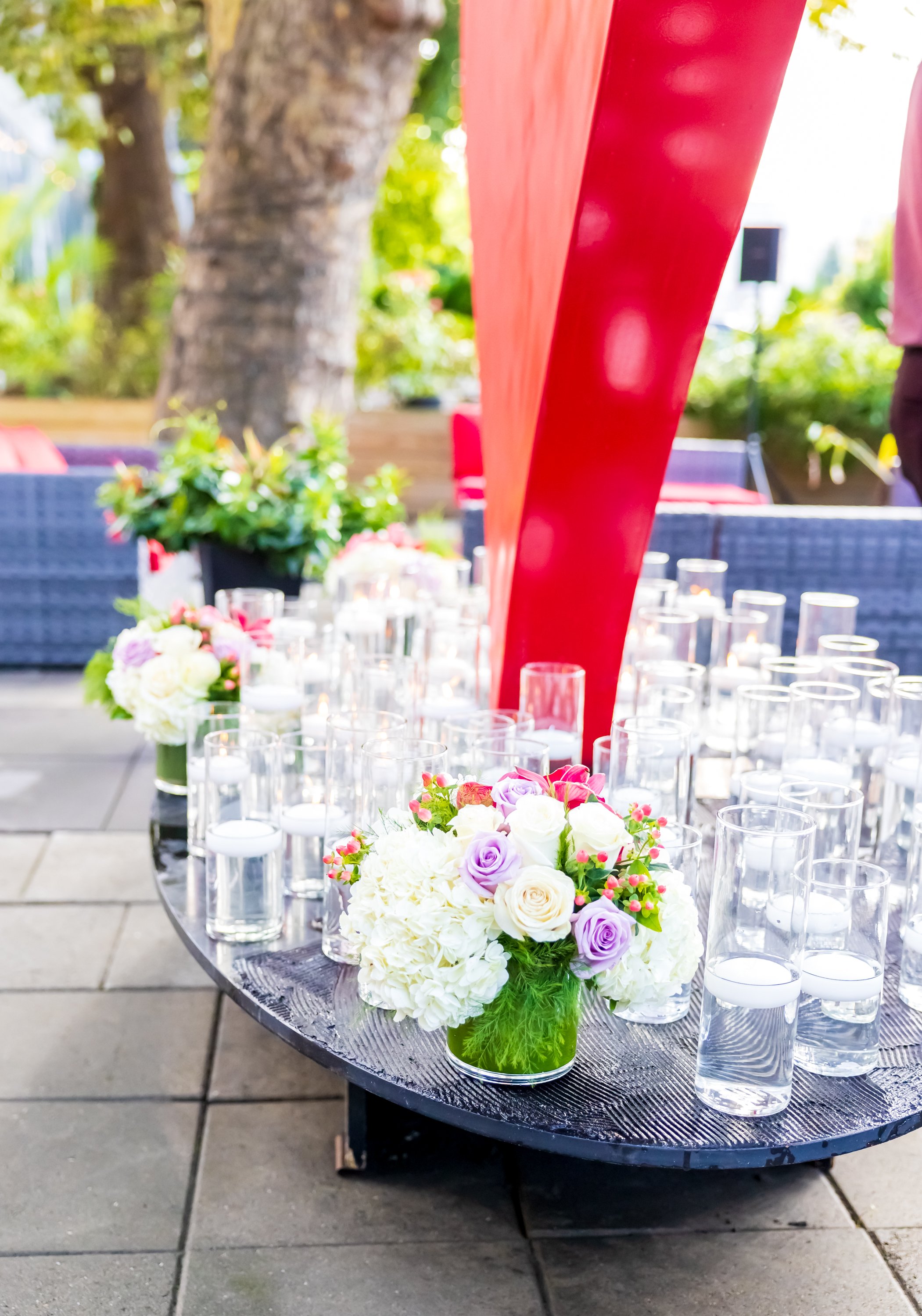 Table with floral arrangements and numerous glass candles at an outdoor event