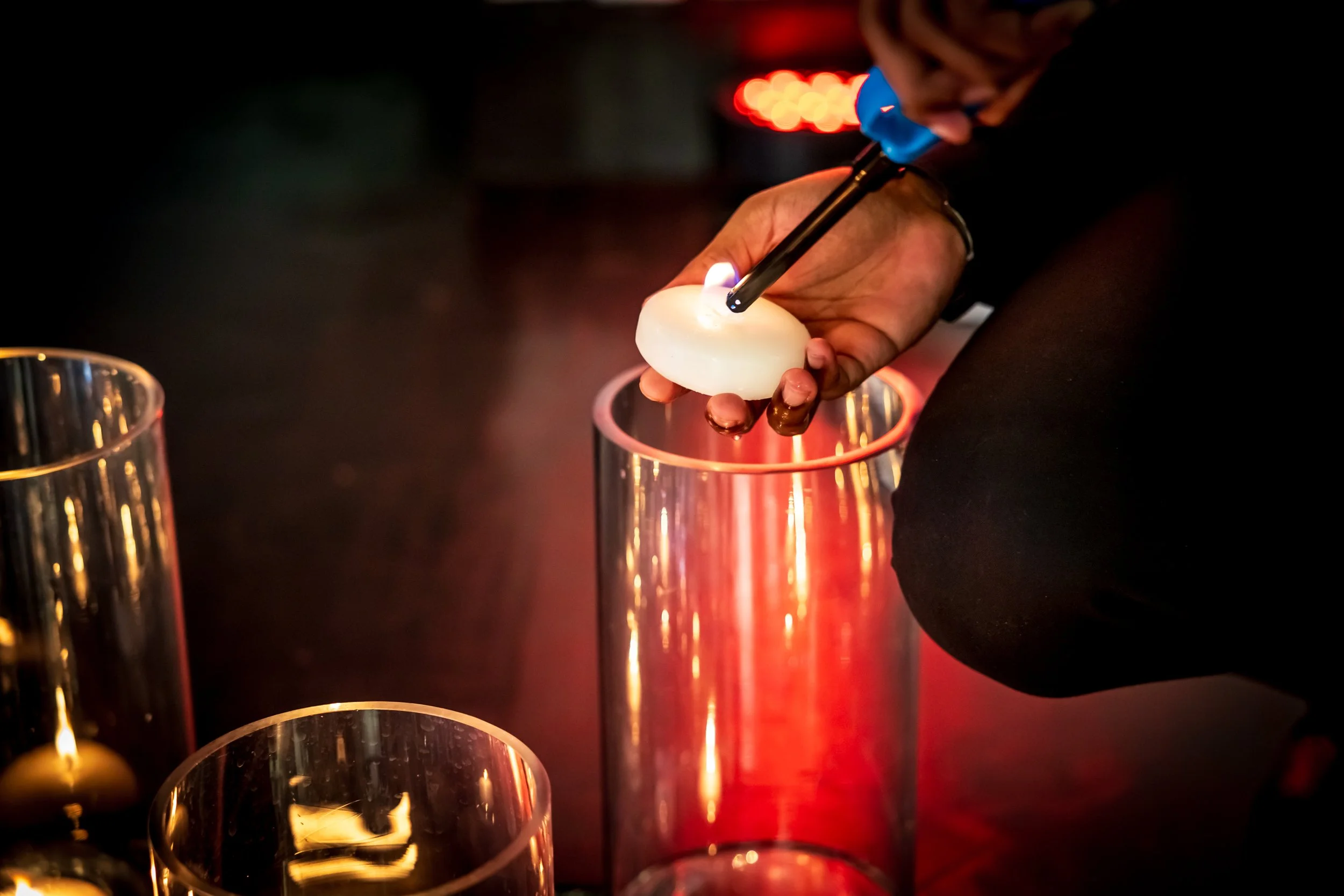 A person using a blowtorch to melt a white object, possibly wax, over a tall glass container.