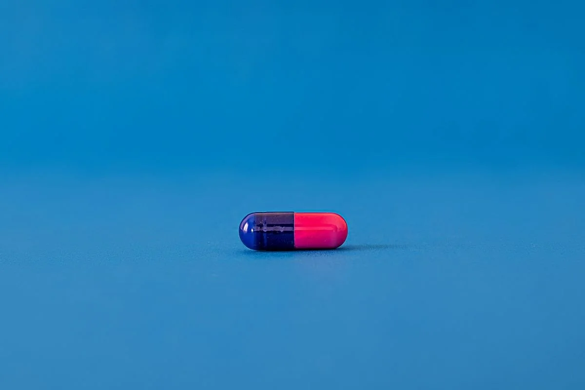 A capsule pill with blue and pink halves on a blue surface.