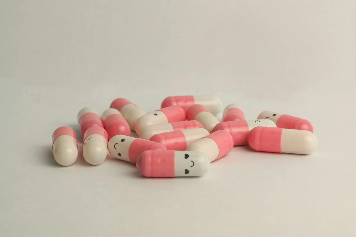 Pink and white capsules with smiling faces and small hearts on a plain white background.