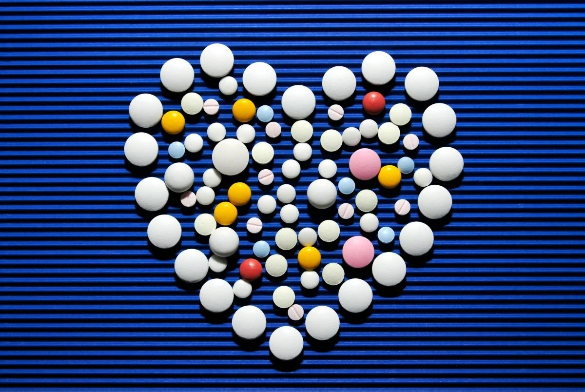 Colored pills and tablets arranged in a heart shape on a blue ribbed background.