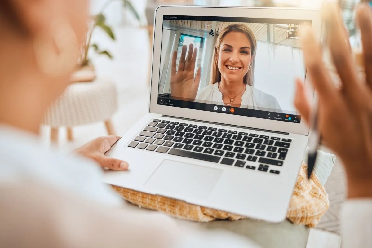 Person having a video visit with their therapist on a laptop, smiling and waving at the camera.