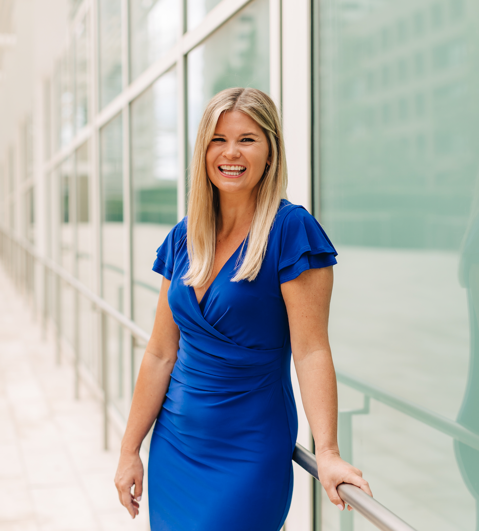 Career Coach, Kate Rosenberg, wears a blue dress standing in downtown San Diego next to an office building outdoors, smiling warmly.