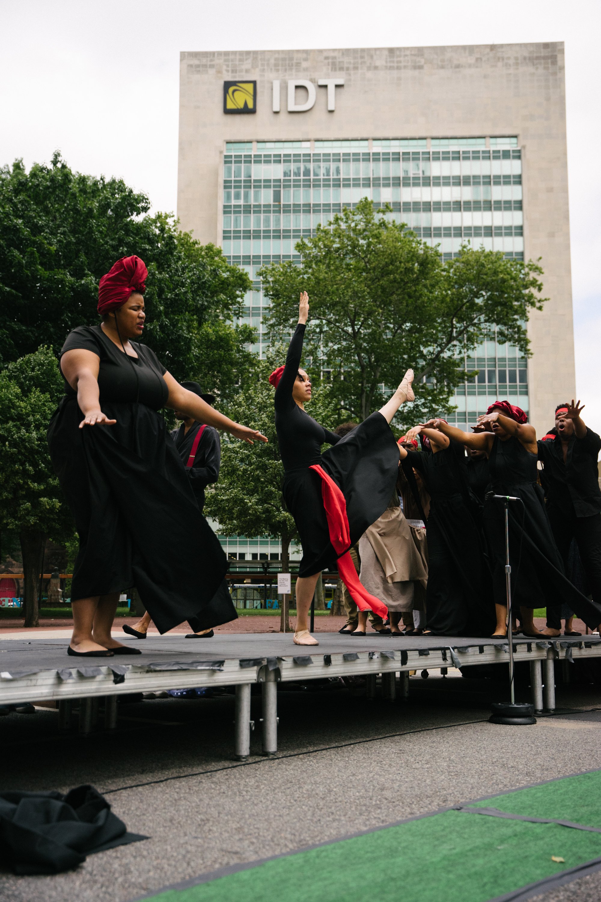 Photo by Bryon Summers
Alneesha Moret Harris is downstage singing with her arms spread in front of her. Sol Lecour dances center with their left leg and right arm raised to the air. Behind them is a sea of Aurway Artist singing behind them. The ID